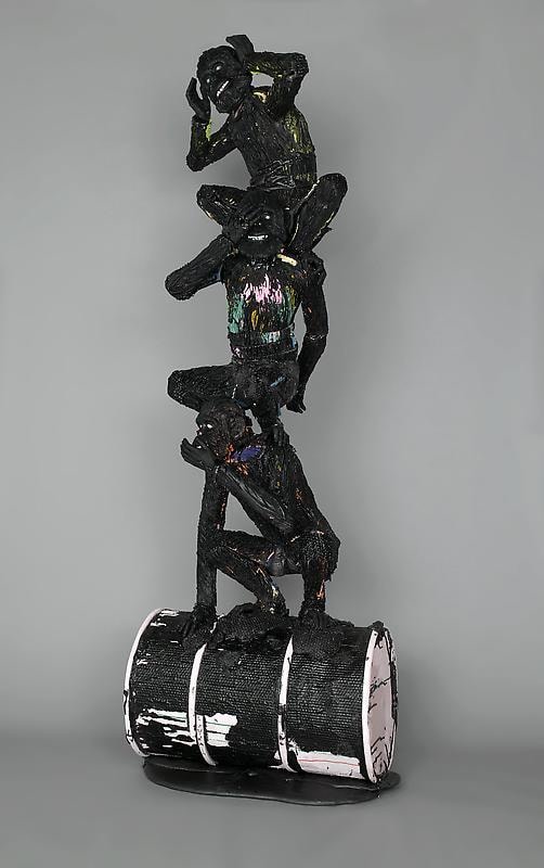 black figures balancing on each other while the lower one stands on a black barrel