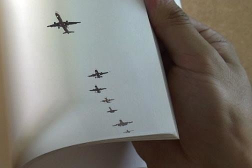 a hand flipping through pages of a book; the current page has airplanes printed on it