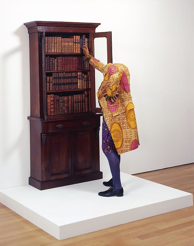 mannequin dressed in a gold jacket reaching out for books on a shelf