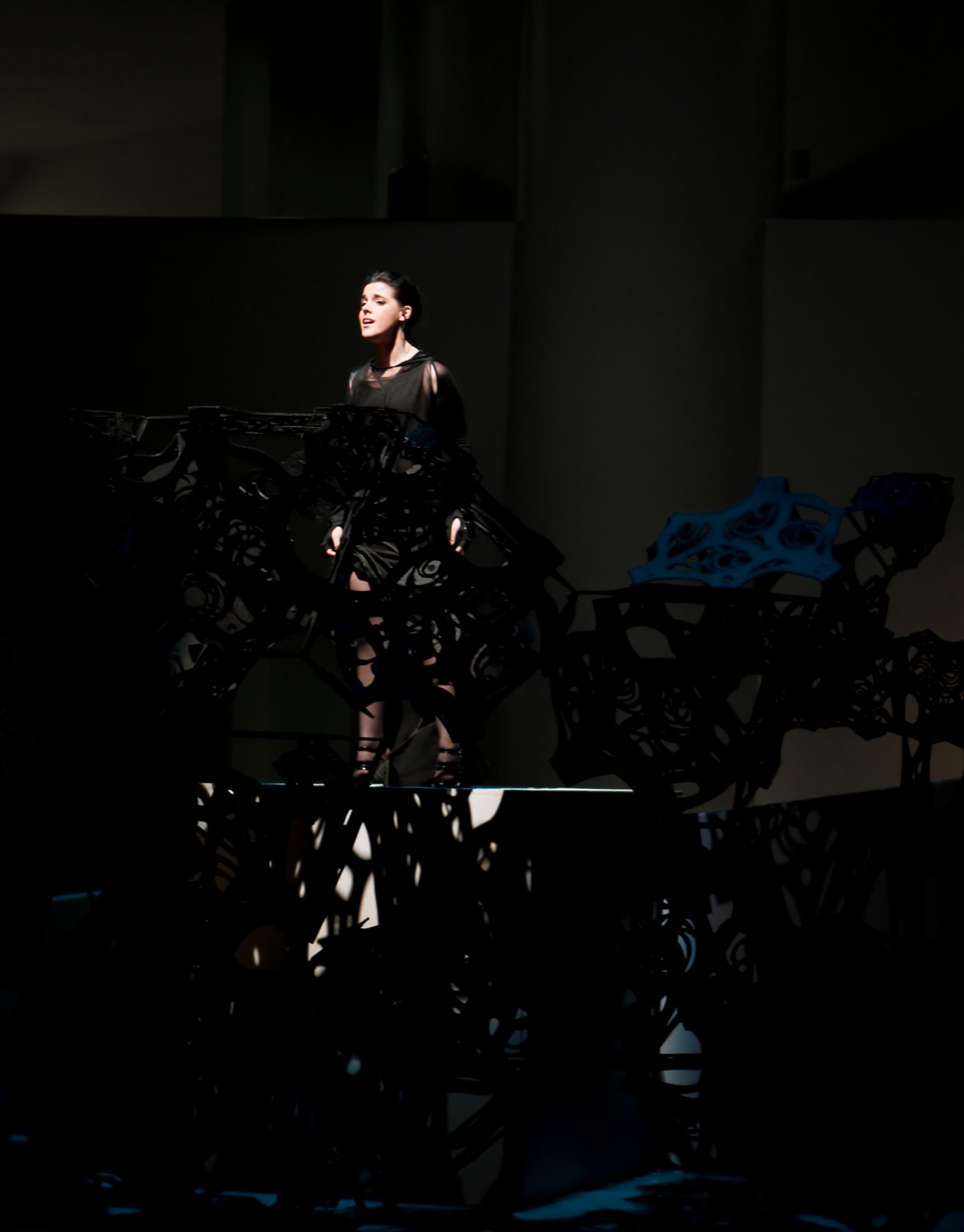 woman in a black leotard standing behind a black, see-through sculpture composed of geometric shapes