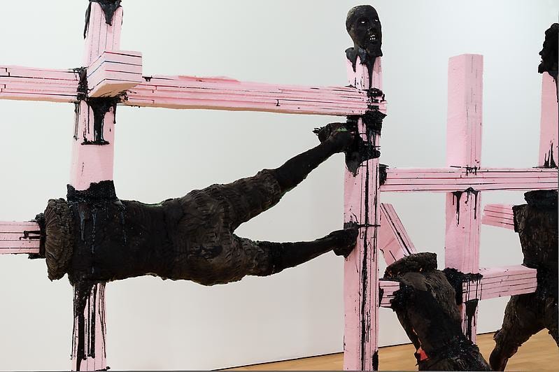 sculpture of bodies covered in black paint with pink beams protruding from them