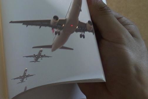 hand flipping through pages of a book; the current page has pictures of airplanes