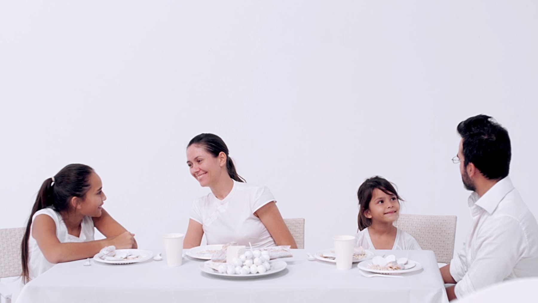 Family dressed in white in an all white room sitting around a white table with white food