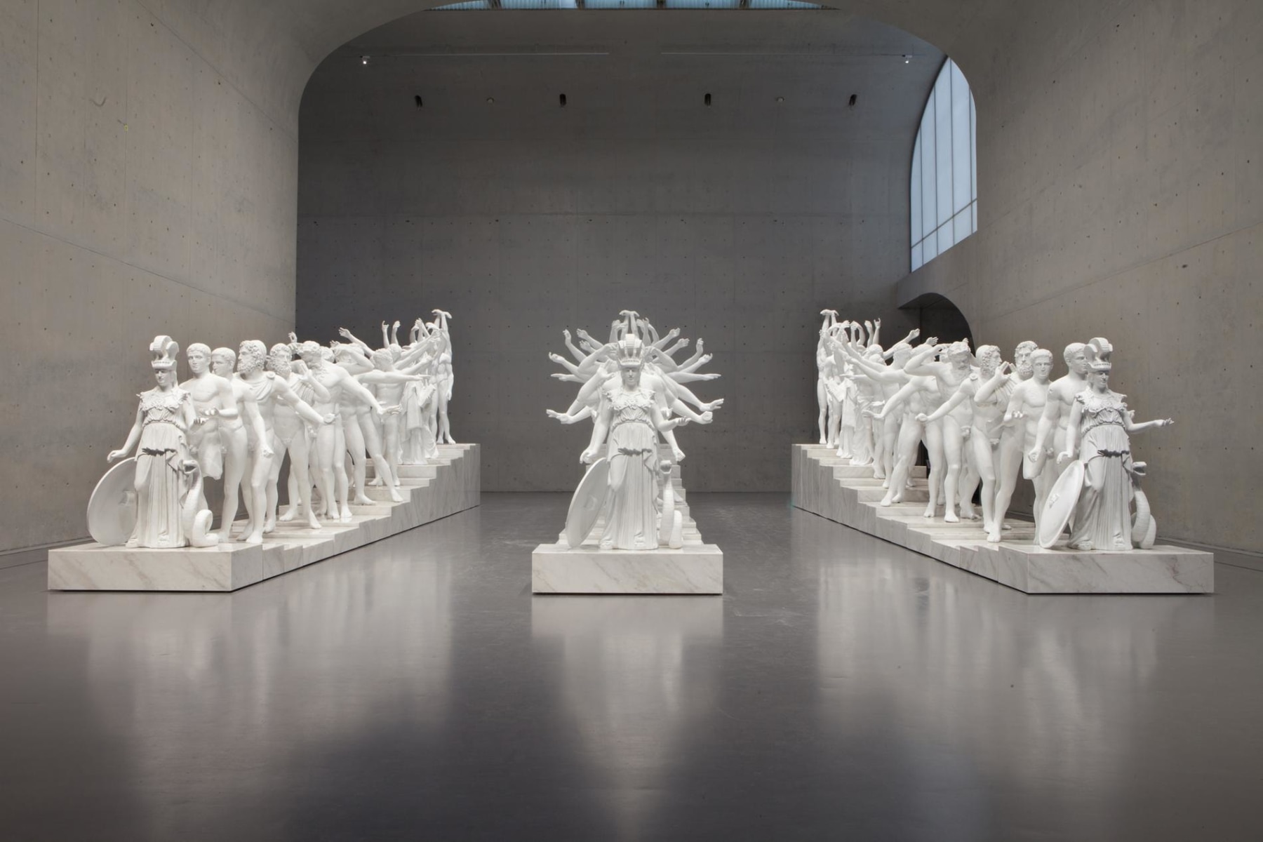 A series of 19 white casts of classical statuary, in three rows, within a large grey room