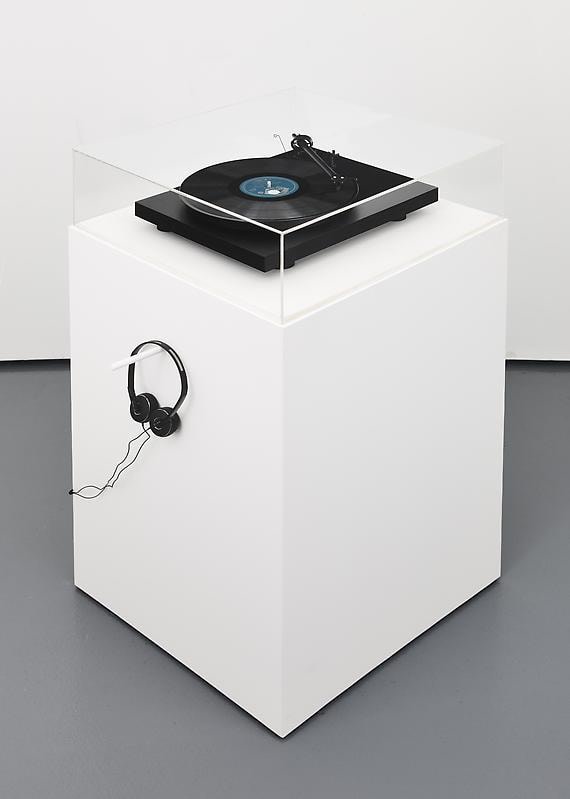 record player encased on a pedestal; a pair of headphones is hanging from one of the pedestal's sides