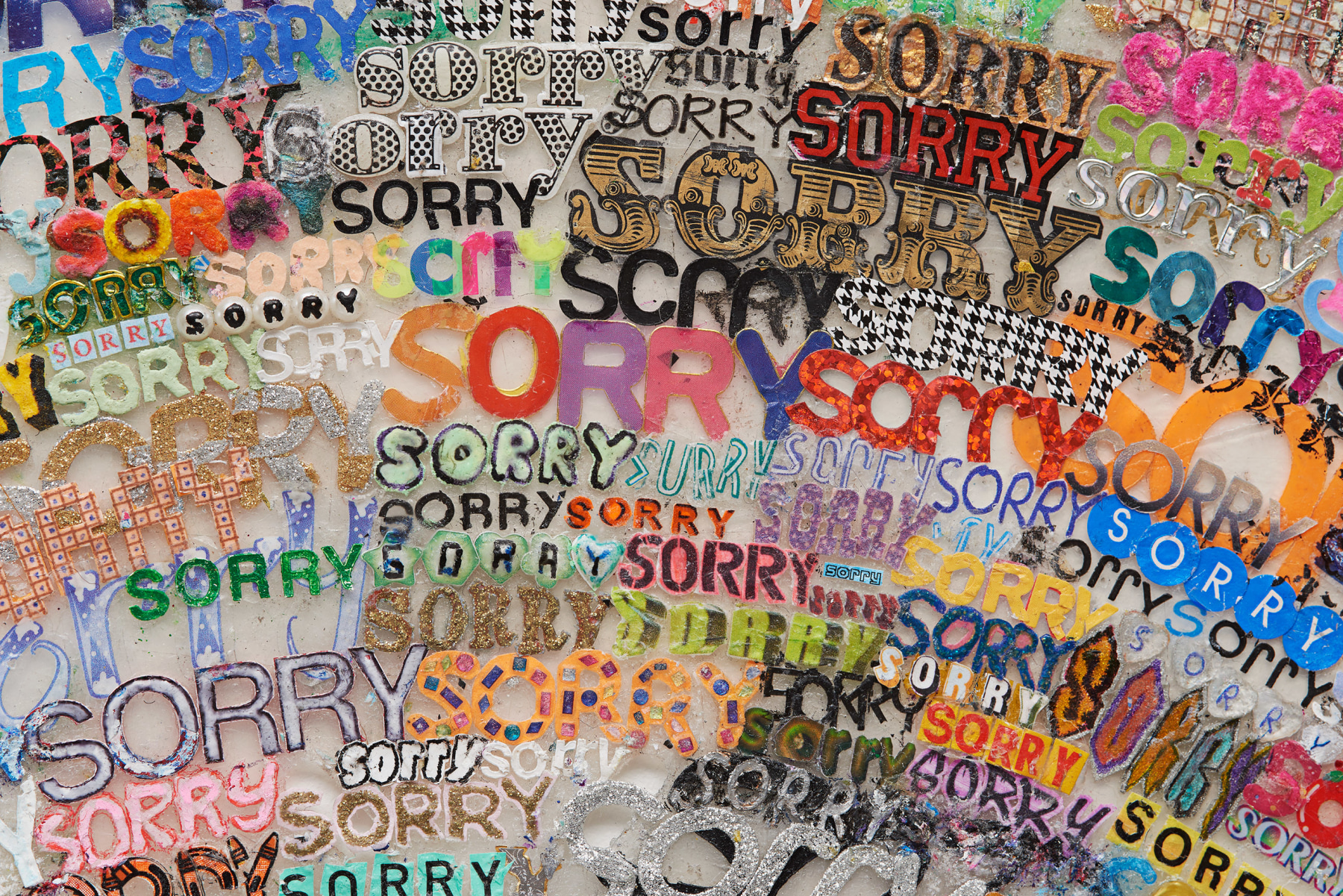 Detail image of a collaged, multimedia depiction of a rainbow composed of the word sorry by SIMON EVANS&trade;.