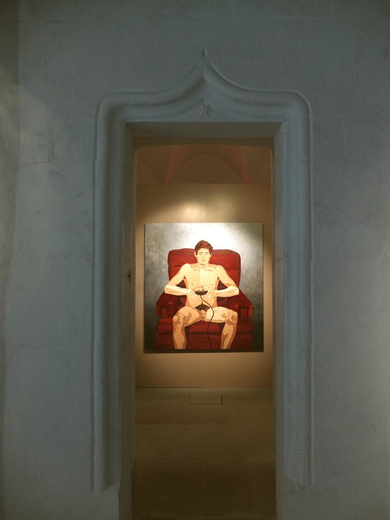 doorway revealing an artwork depicting a nude man sitting a red sofa chair