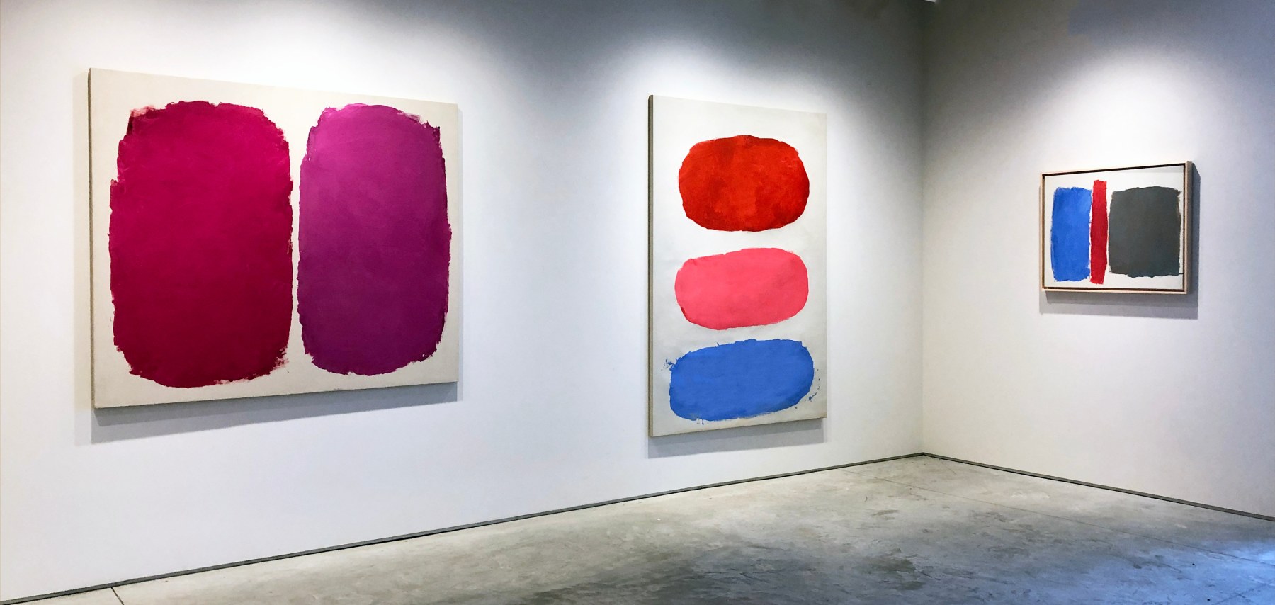 Three paintings by Ray Parker on a white wall in colors of red, pink, purple, blue, grey and orange