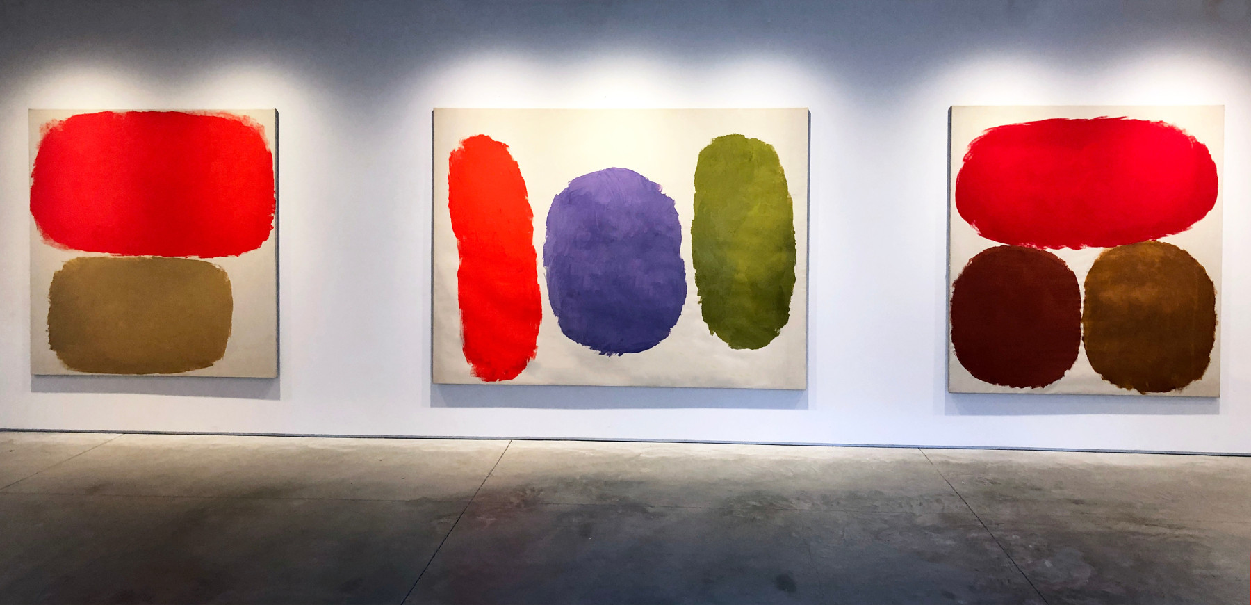 Three paintings by Ray Parker on a white wall in colors of red, brown, green, purple, brown, yellow ochre, and umber