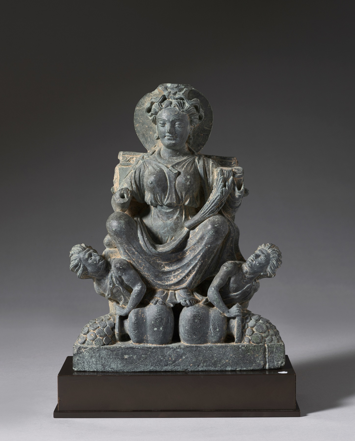 The goddess of abundance and fertility is seated on a throne with her feet resting on two overturned pots. 