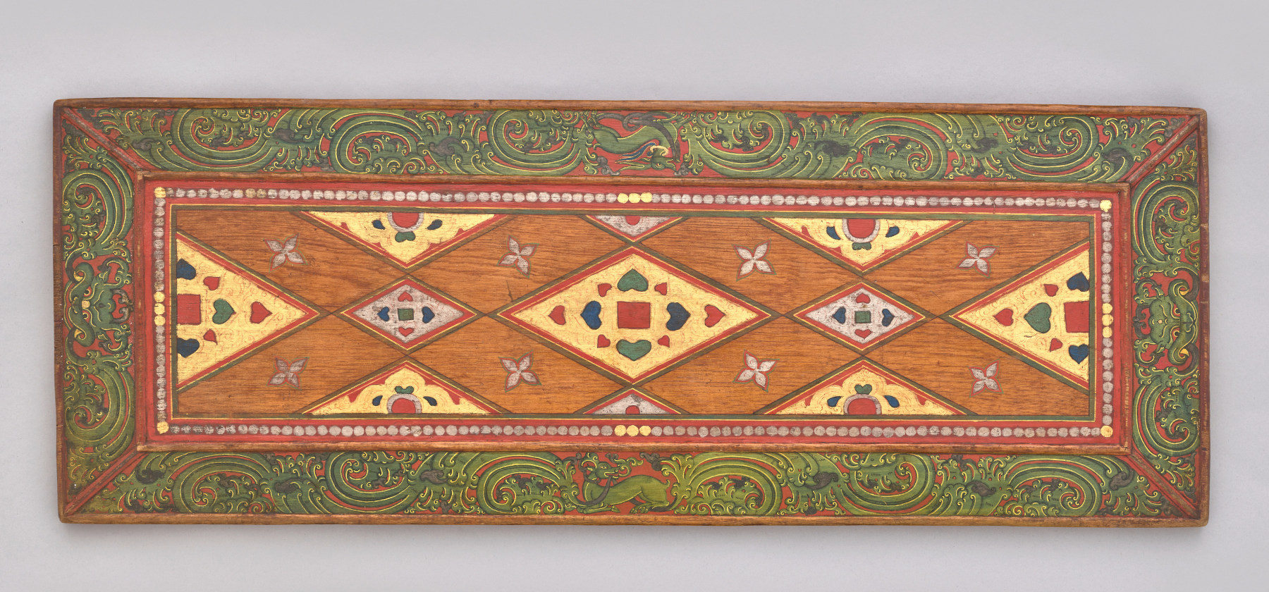 Carved wood and polychrome book cover with jewel-encrusted shapes and flowing scroll work on the edges
