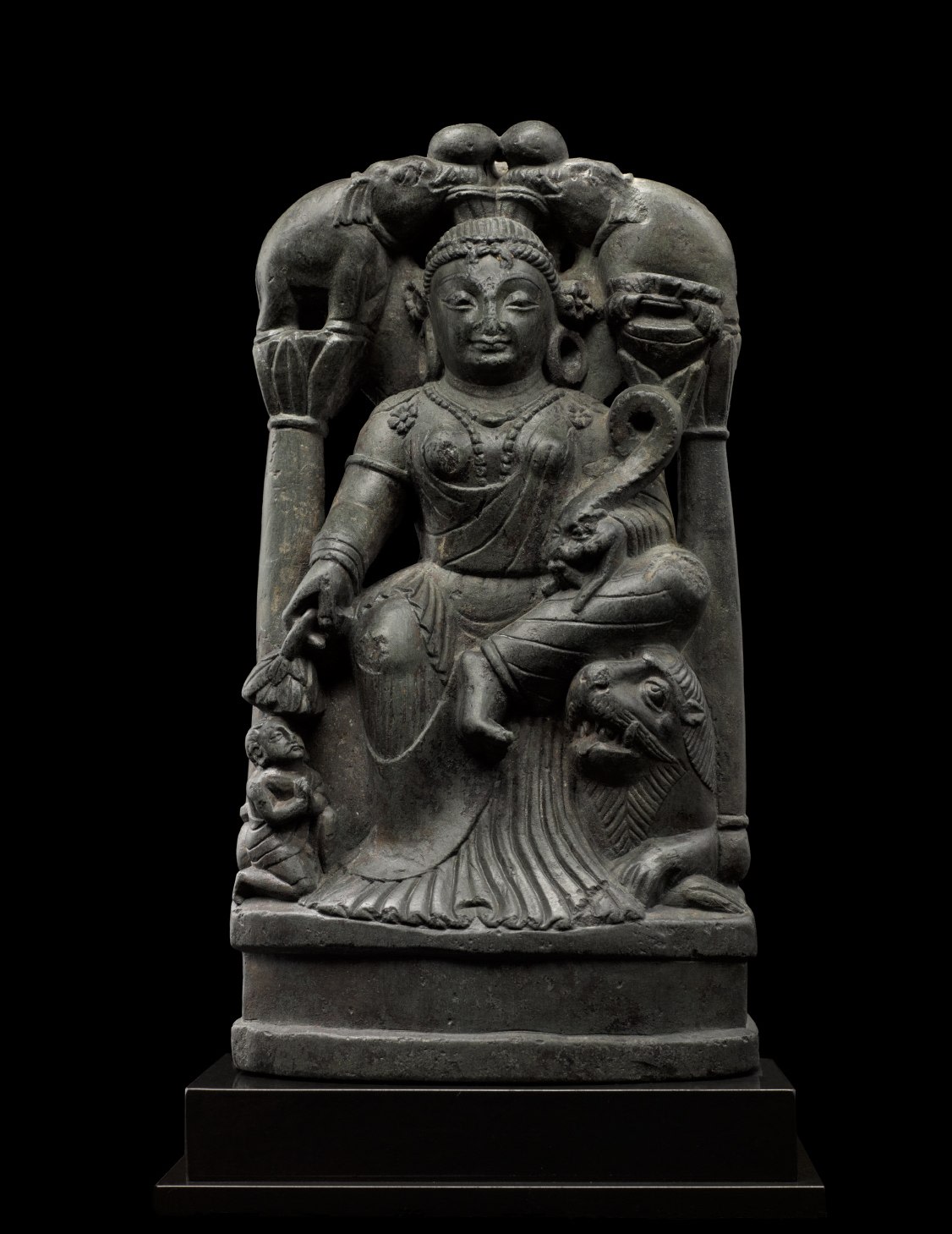 Large photo of Sculpture of Gaja Lakshmi, the Goddess of Fortune, who is venerated as a bringer of good fortune and well-being to the earth, of which she was an early personification.  She wears a long transparent chiton with delicate pleats pooling on the base, beaded jewelry, large hoop earrings, and stylized mural crown. 