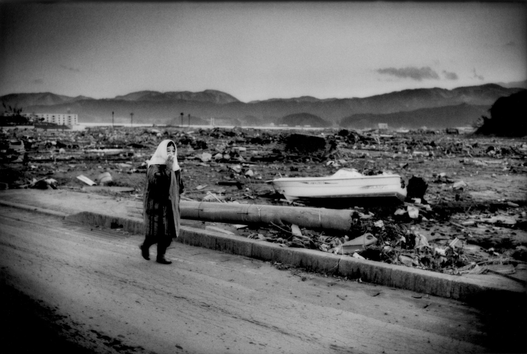 Resident of Rikuzen-Takata walks at the high water mark of the great tsunami several kilometers from the sea and still lumber is piled up on rooftops, Rikuzen-Takata, Iwate Prefecture, Japan, 2011