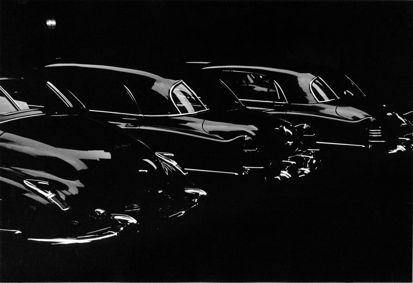 Dark black and white photo showing light glinting on parked cars from the 1040s and early 50s.