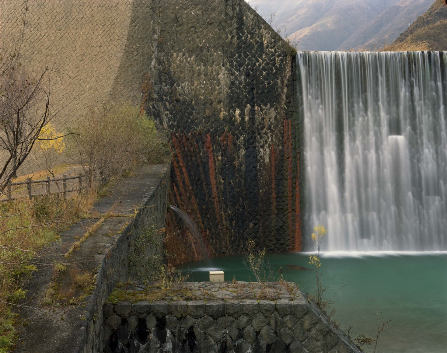 Color photogrpah of water spilling over a dam and into a reservoir.