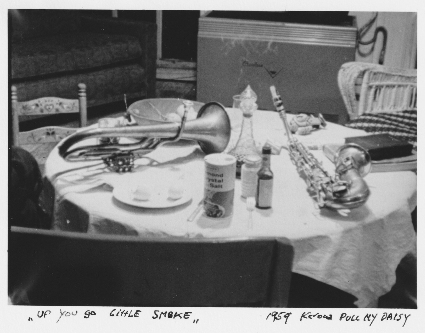 Black and white photo of an alto saxophone and a tenor horn on a kitchen table with a canister of salt and other condiments.