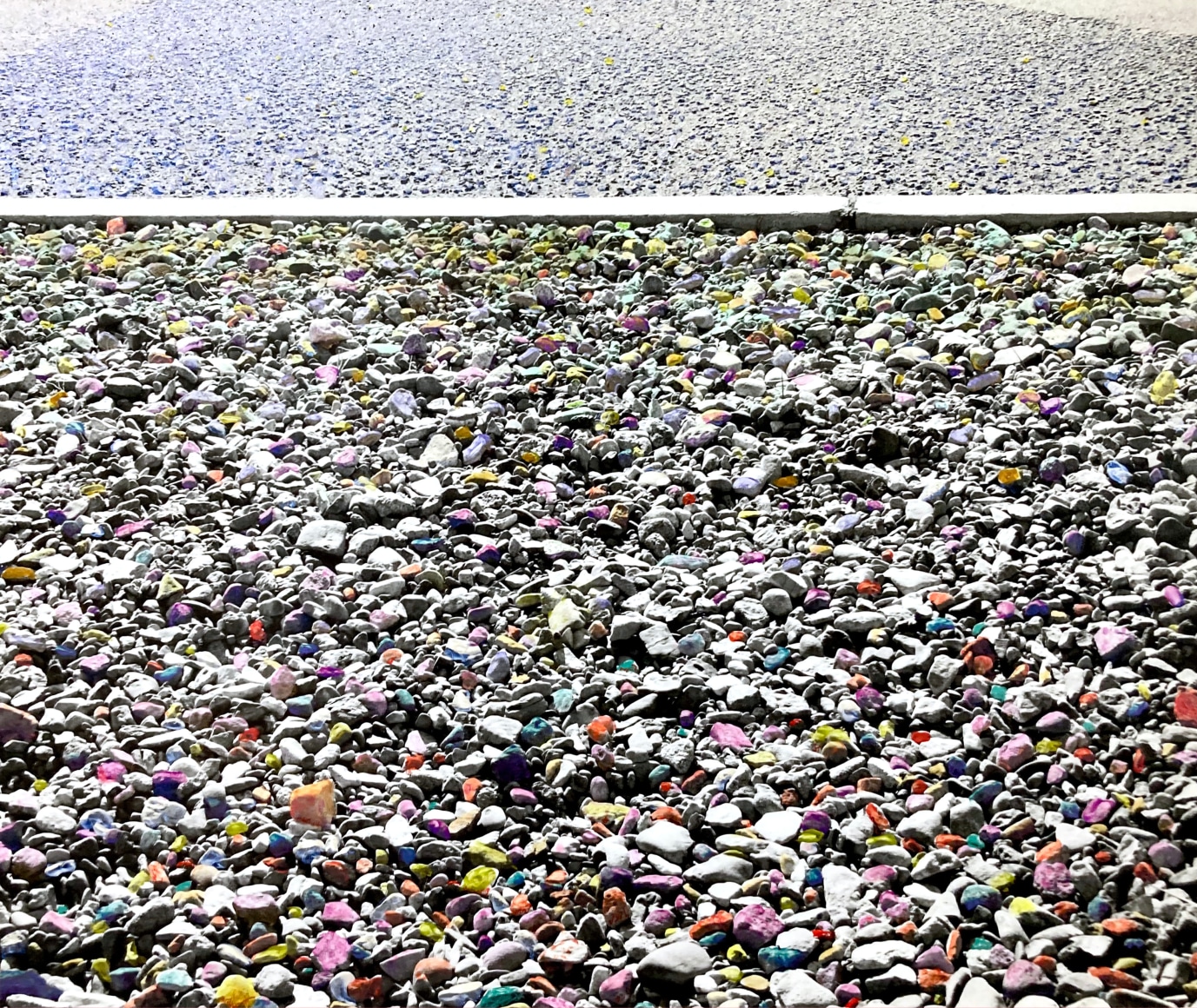 Black and white photo of a field of small stones, the stones are painted different colors on the photo print