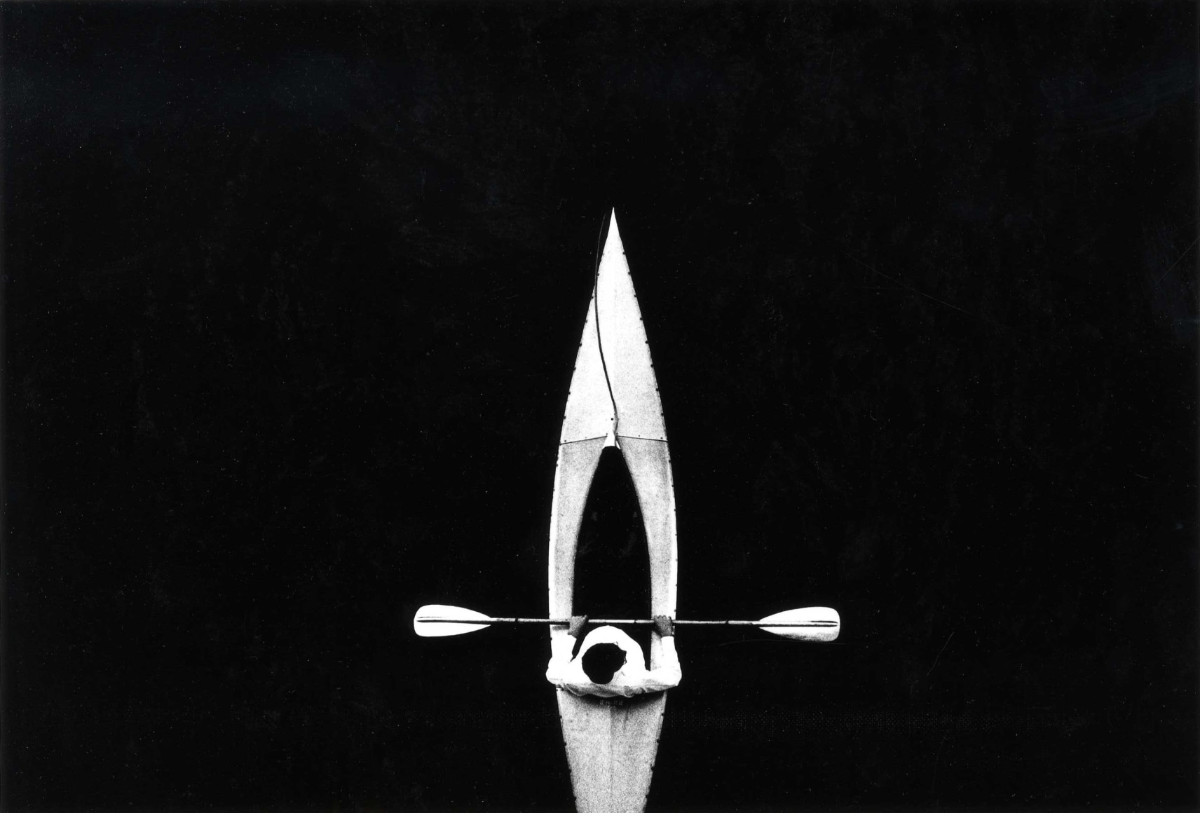 High contrast black and white image of a man in a kayak, seen from directly above.