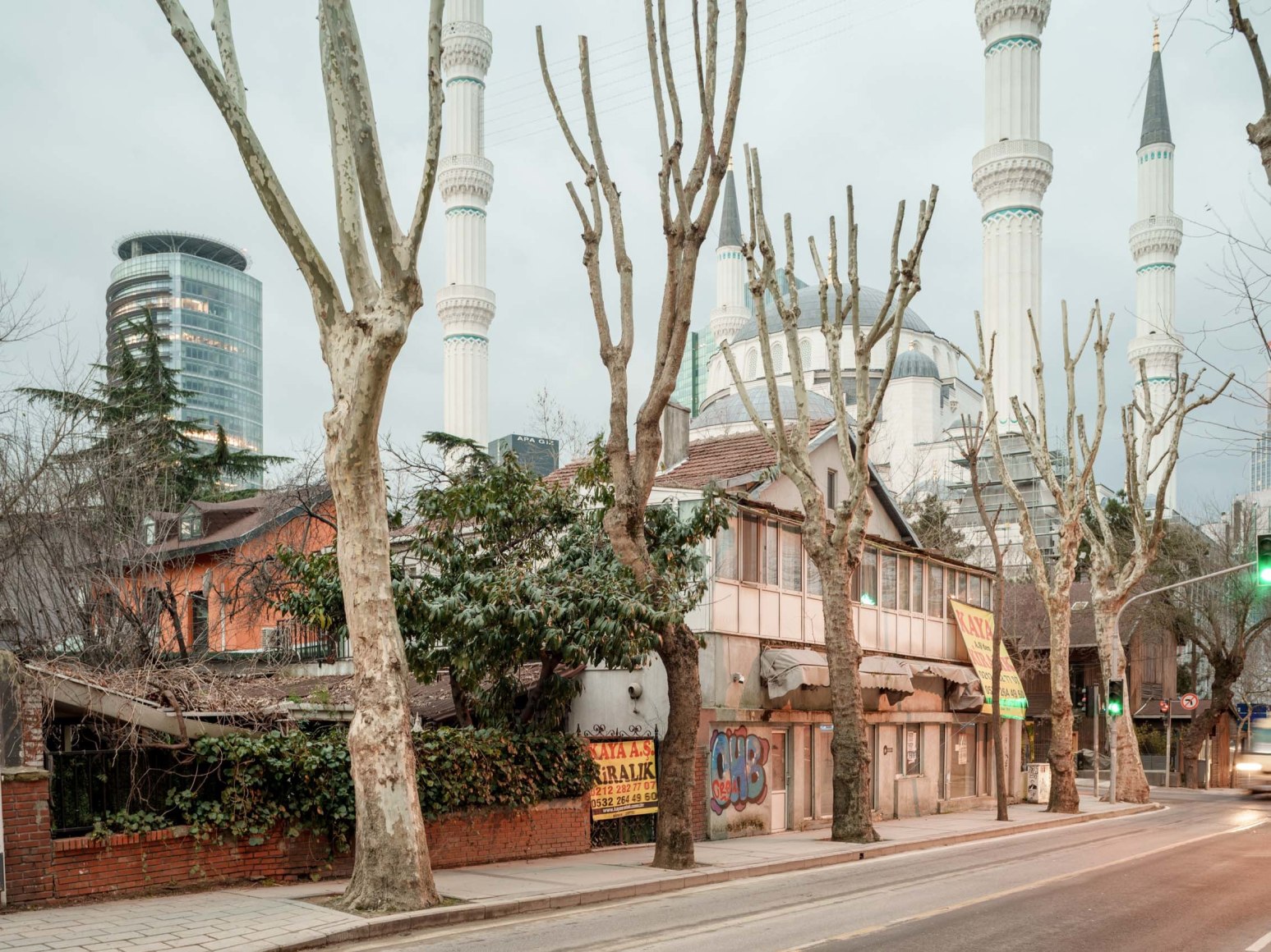 Color photo showing a city street in Istanbul, a mosque is in the foreground and modern glass towers are seen in the background.