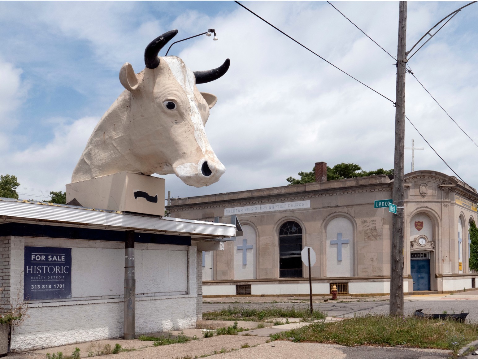 Color photo of a large bull head statue on top of a closed business in an urban neighborhood.