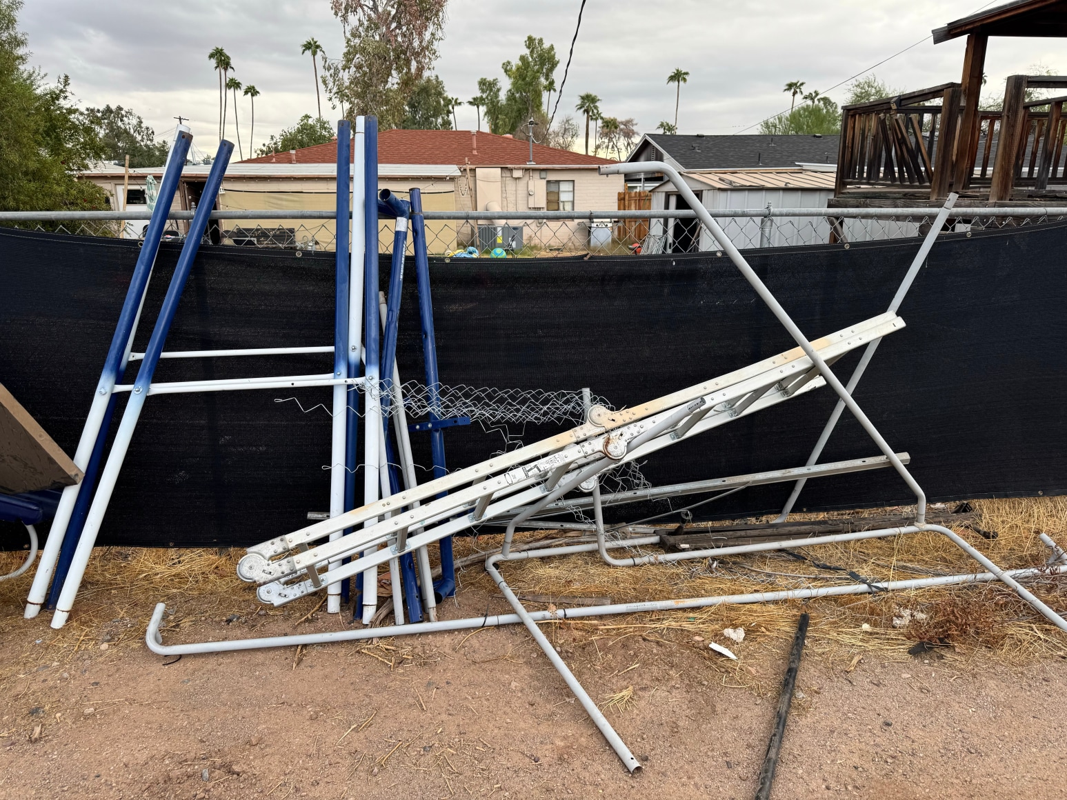 Color photo os discarded metal items piled against a fence in a backyard in the Southwest.