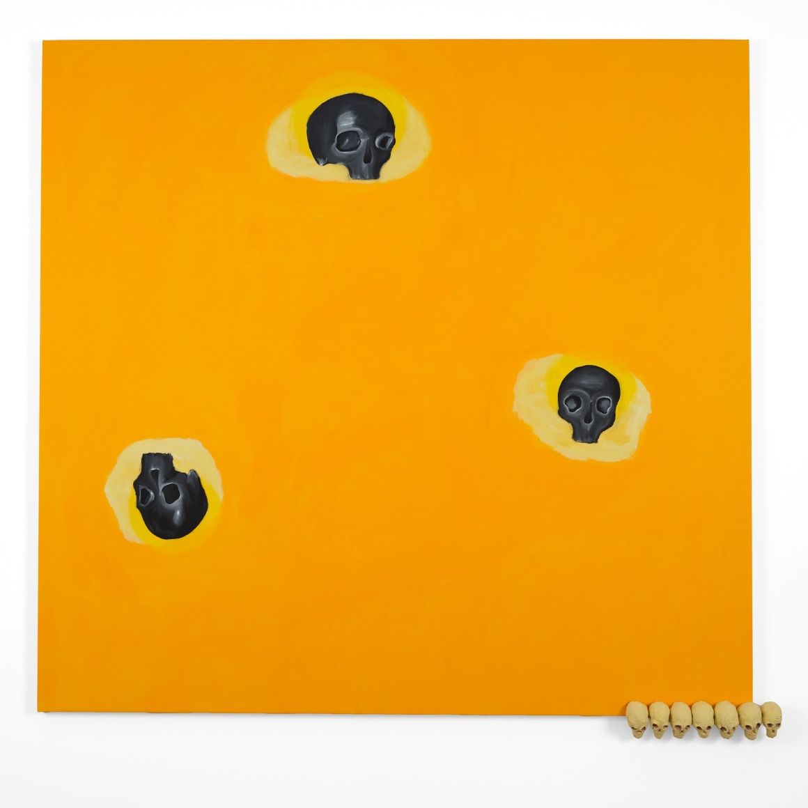 yellow painting with skulls and a row of ceramic skulls along the bottom right edge