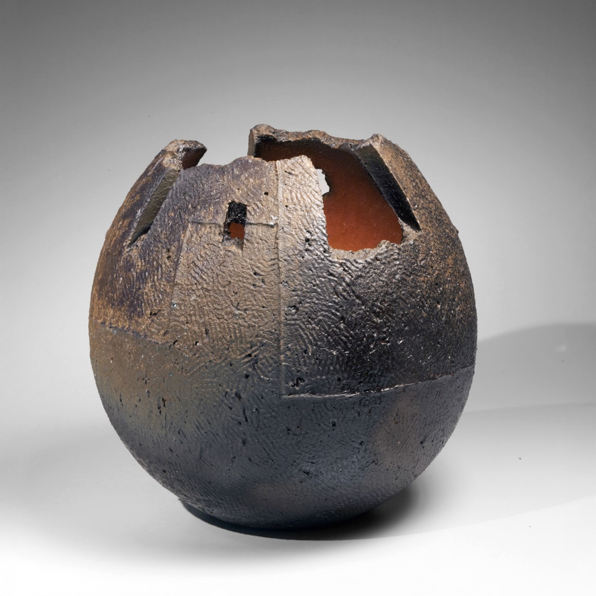 Round dark vessel with textured surface and carved irregular mouth