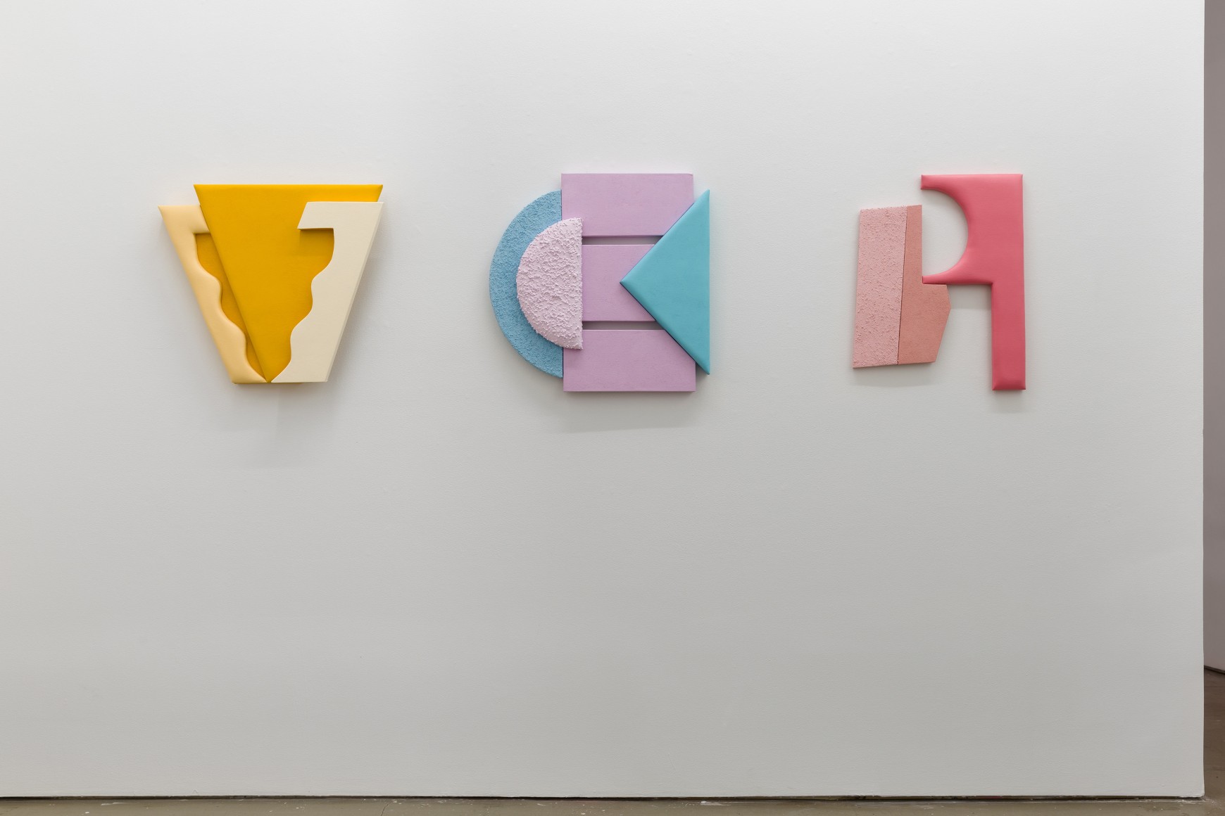 Installation views of Leah Guadagnoli's solo exhibition. Three small geometric sculptures made from fabric, foam, and pumice stone line the walls.