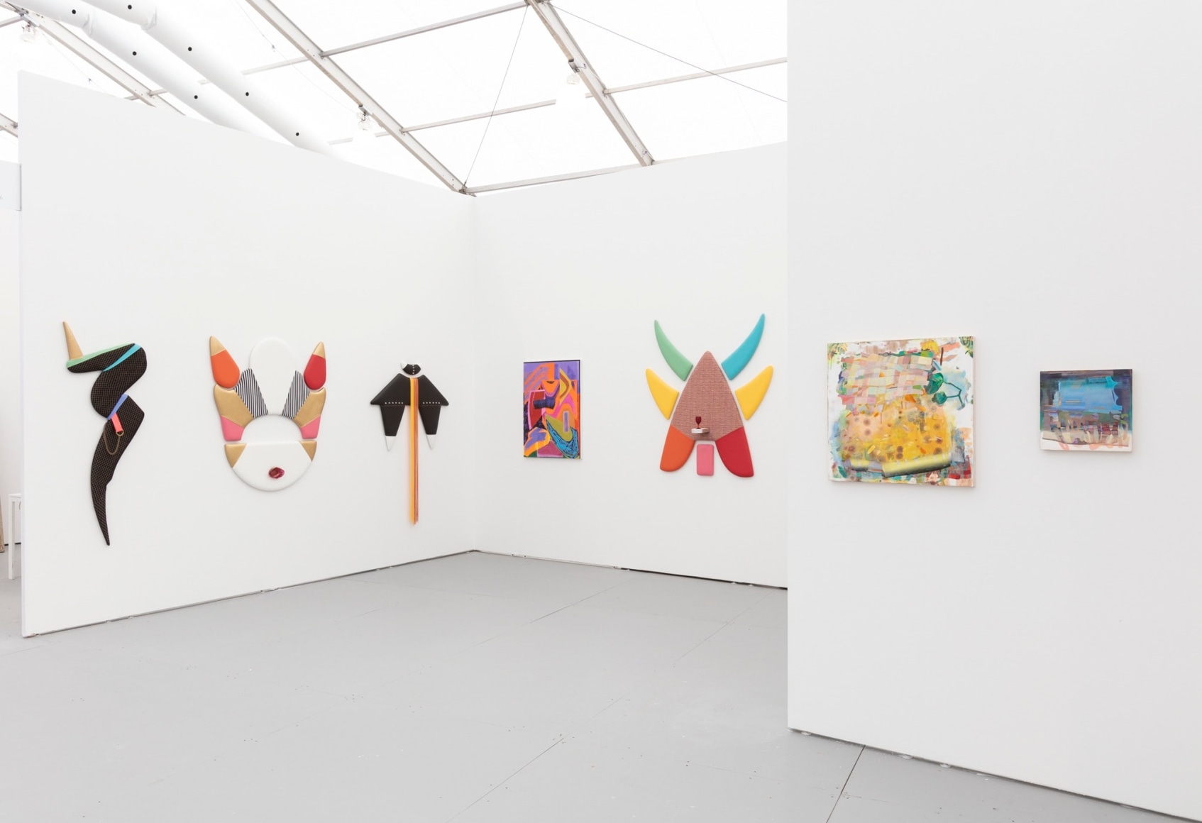 Installation view of an art fair booth, showcasing paintings and flat sculptures on the walls