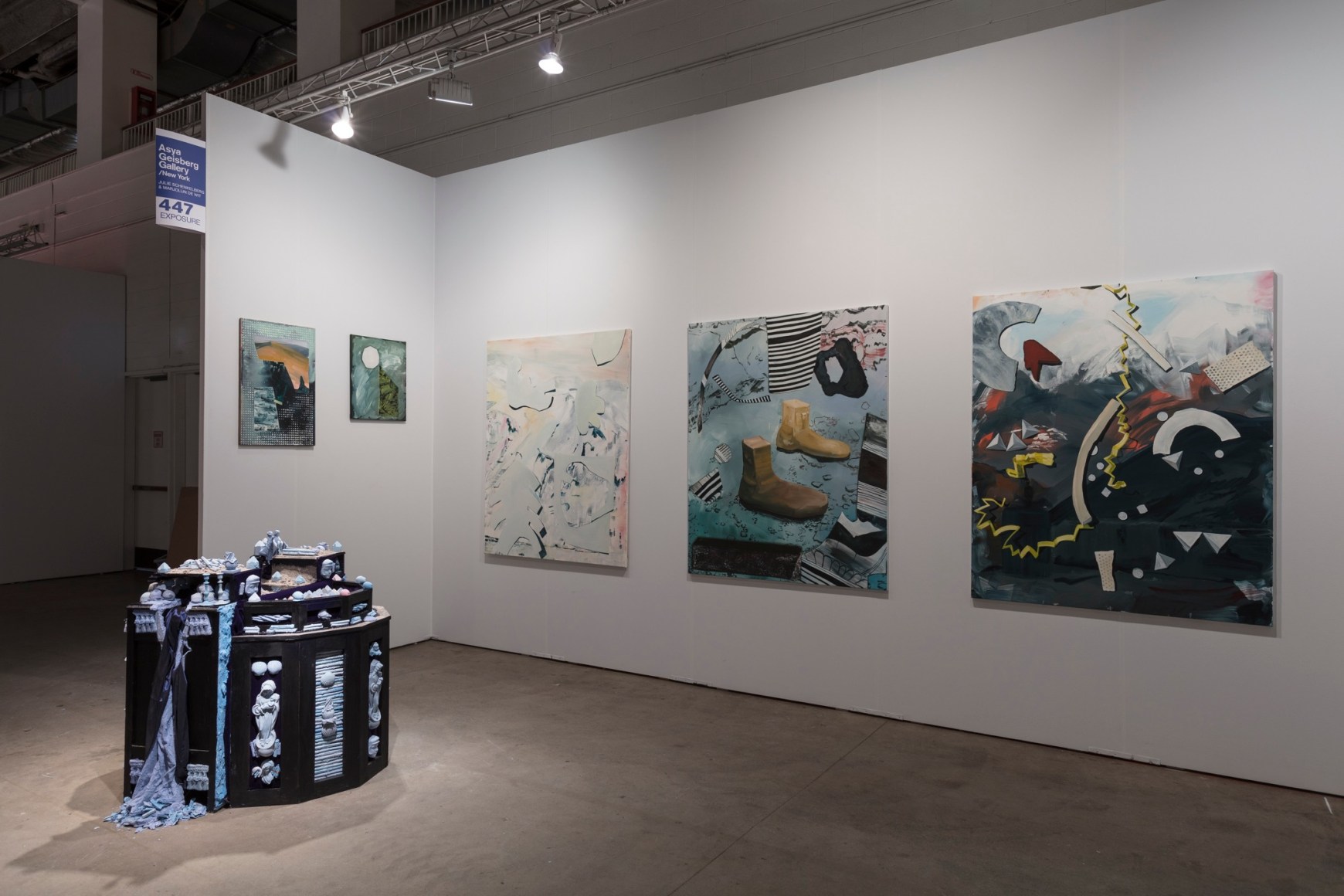 Installation view of an open art fair booth, showcasing artwork on the walls. A large &quot;wishing well&quot; installation is on the floor.