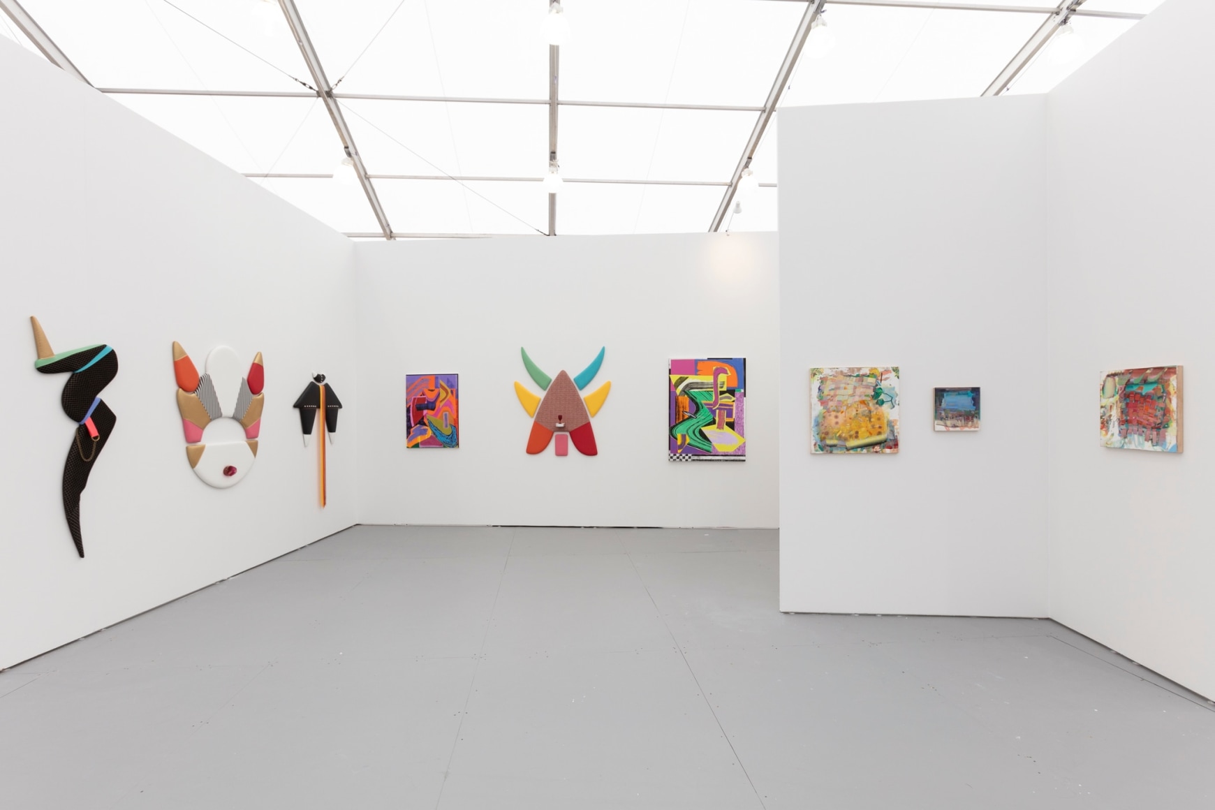 Installation of an art fair booth, showcasing paintings and flat sculptures on the walls