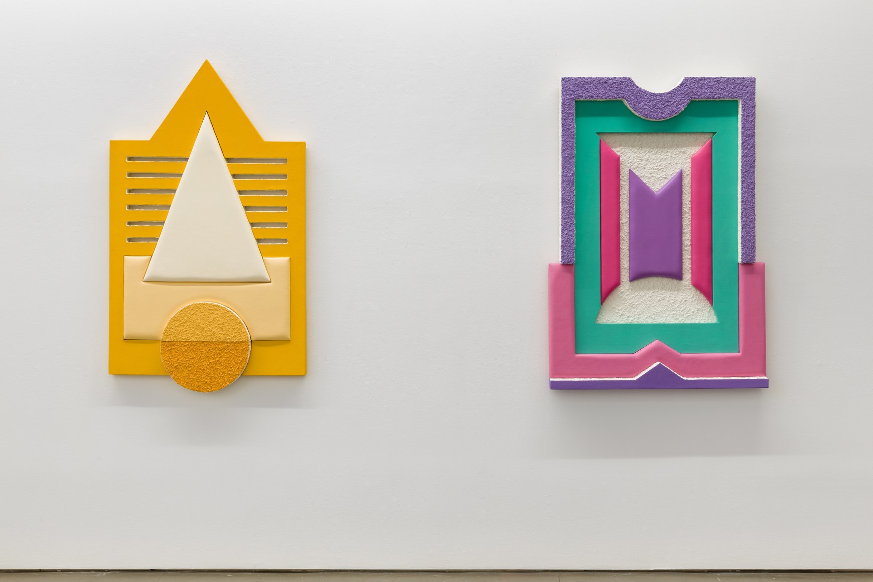 Installation views of Leah Guadagnoli's solo exhibition. Two geometric sculptures made from fabric, foam, and pumice stone line the walls.