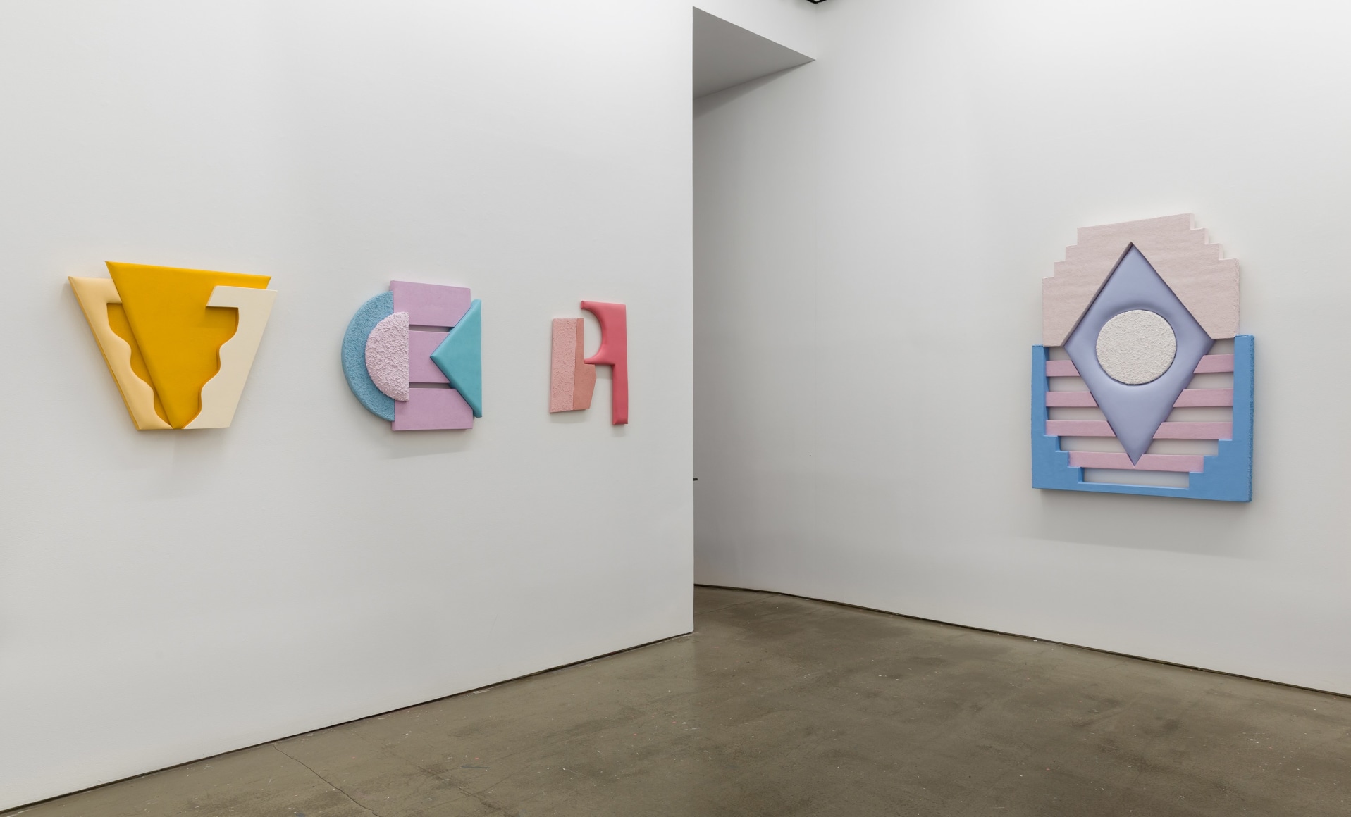 Installation views of Leah Guadagnoli's solo exhibition. Geometric sculptures made from fabric, foam, and pumice stone line the walls next to a doorway.