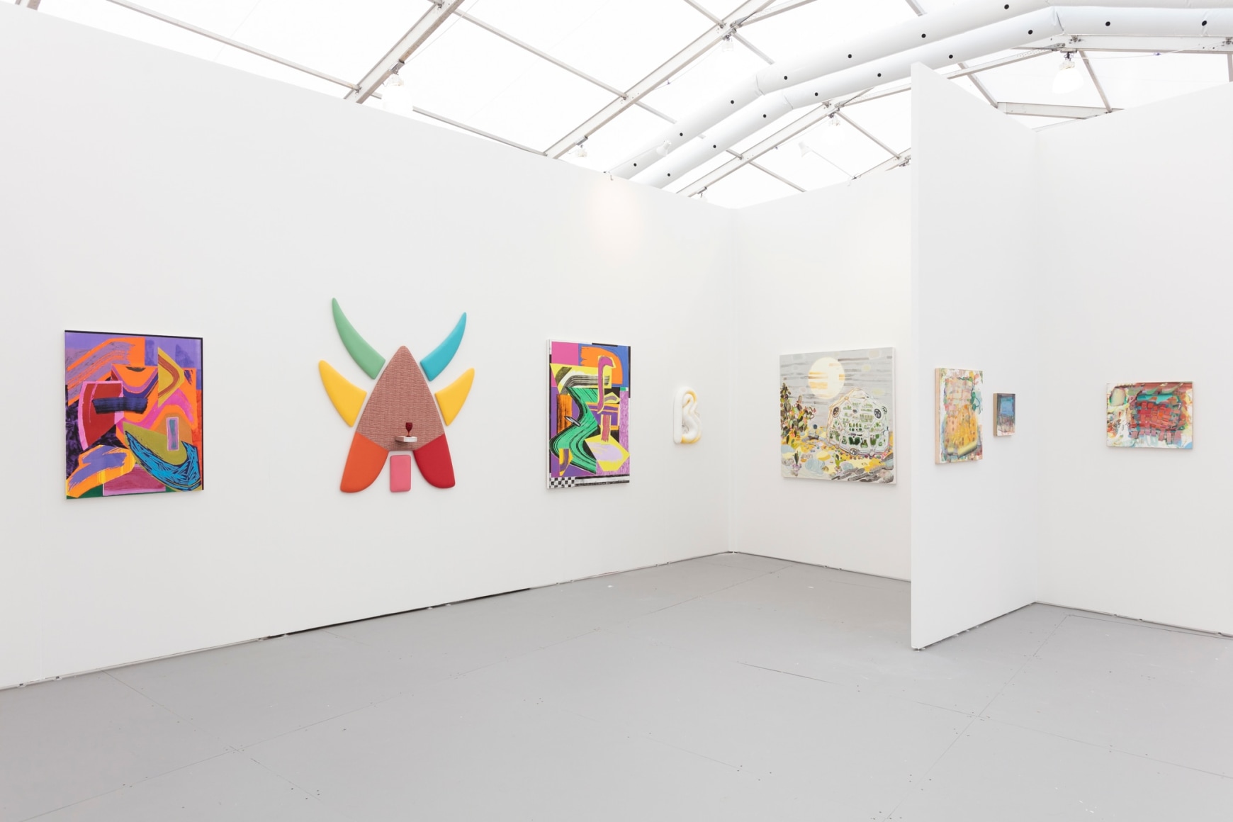 Installation view of an art fair booth, showcasing paintings and flat sculptures on the walls