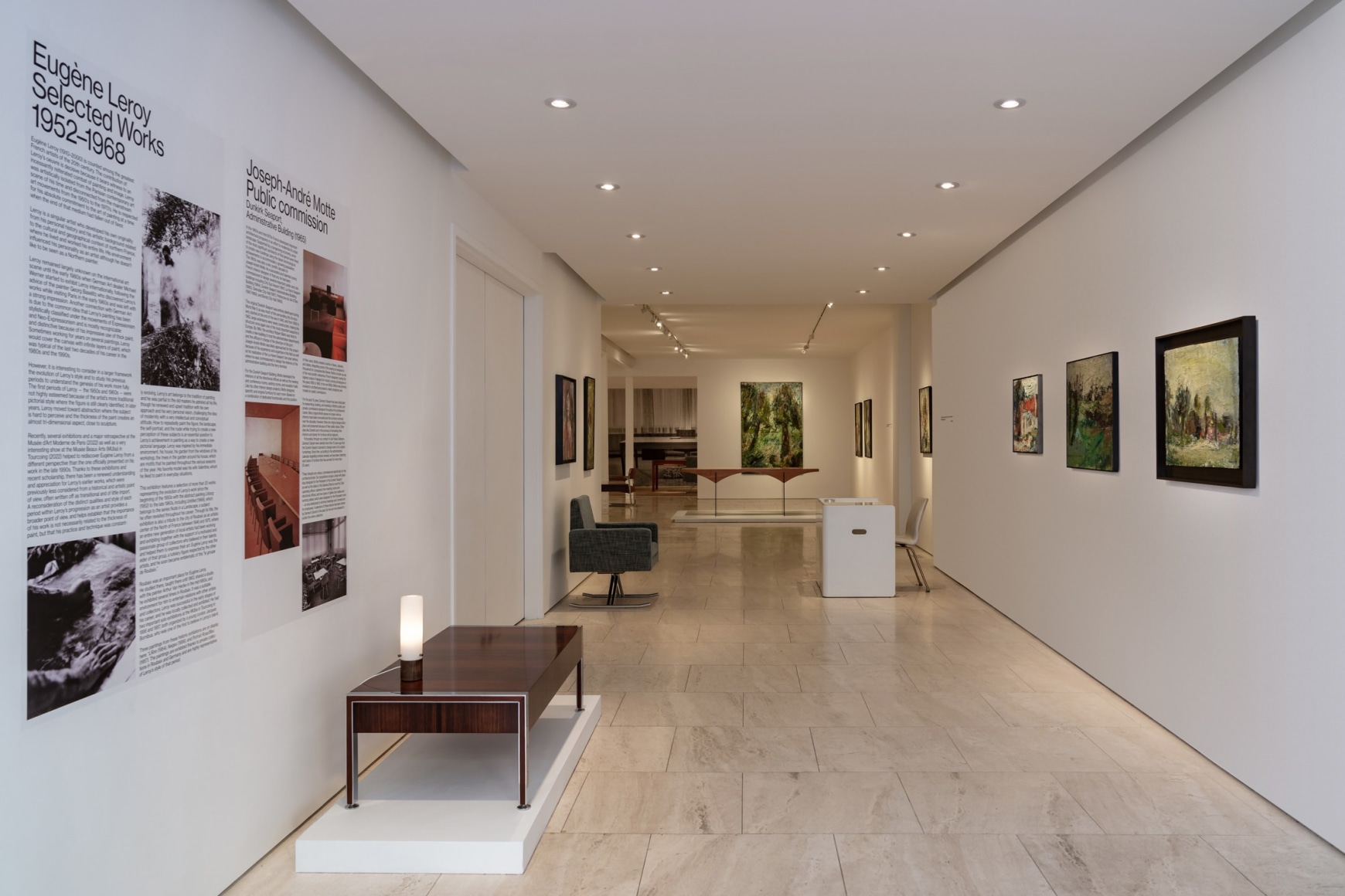 Exhibition text describing the designer and artist showing with a low table and light on top with paintings on the opposite wall.