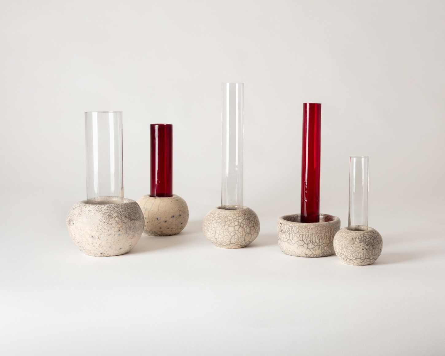 Group of raku and glass vases sitting beside eachother, various heights.