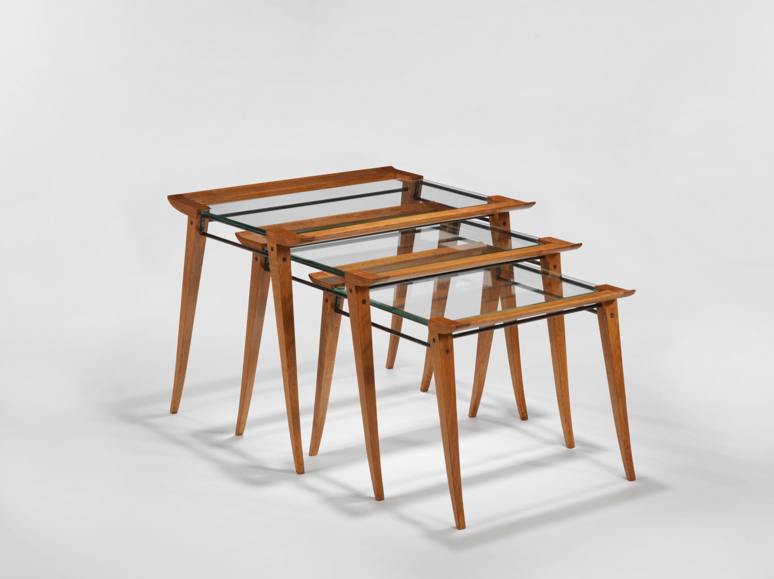 photograph of a set of three nesting tables, legs are made from wood and tops surface is glass