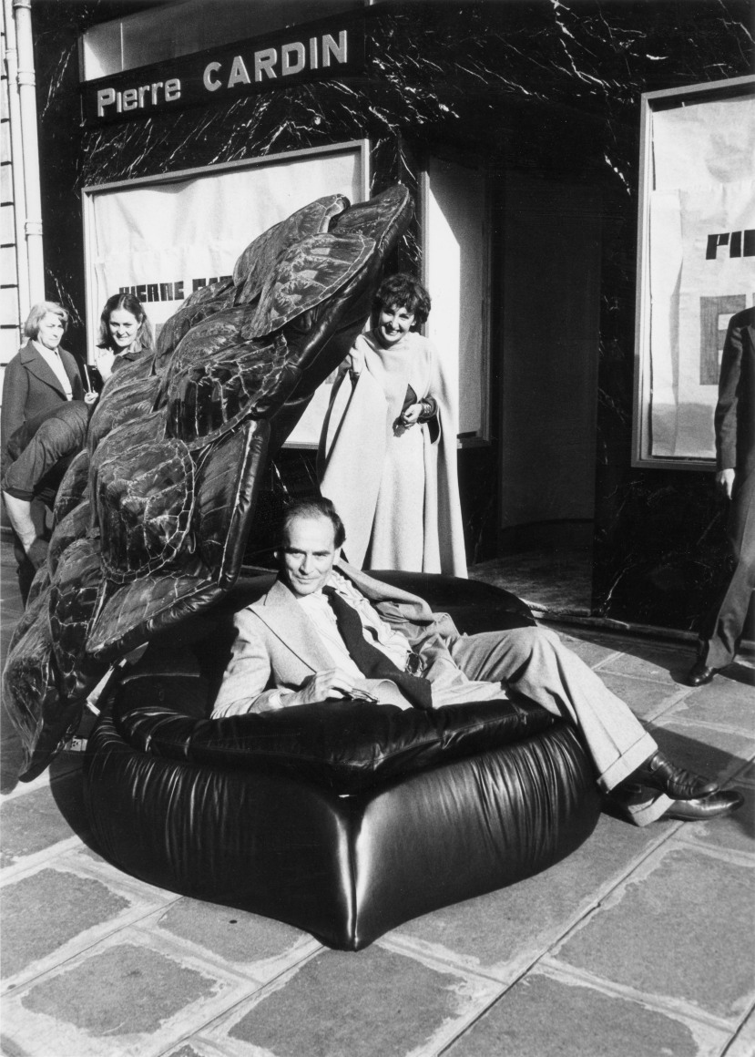 Pierre Cardin inside a couch designed by Maria Pergay who is standing behind him