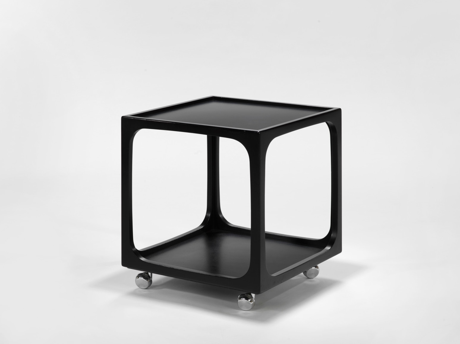 photograph of a small, square, black table with wheels in a blank room