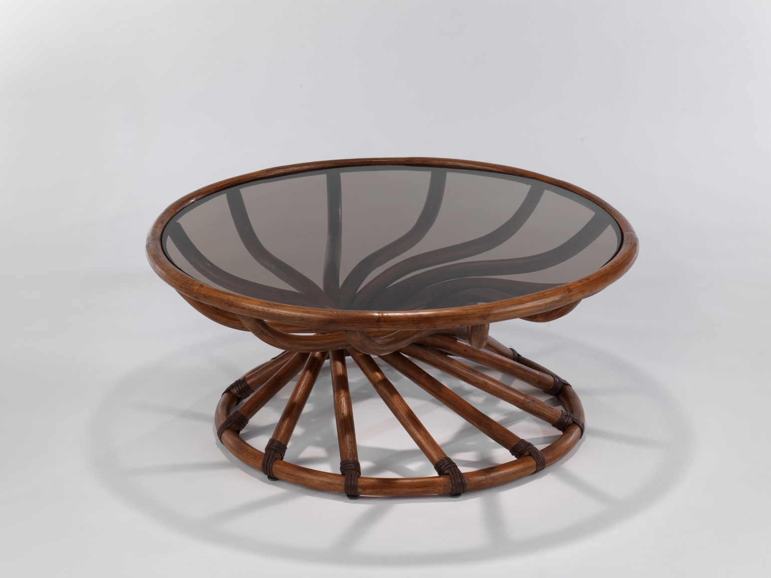 Smoked Glass top low table with curving stained woven bamboo structure in front of white background