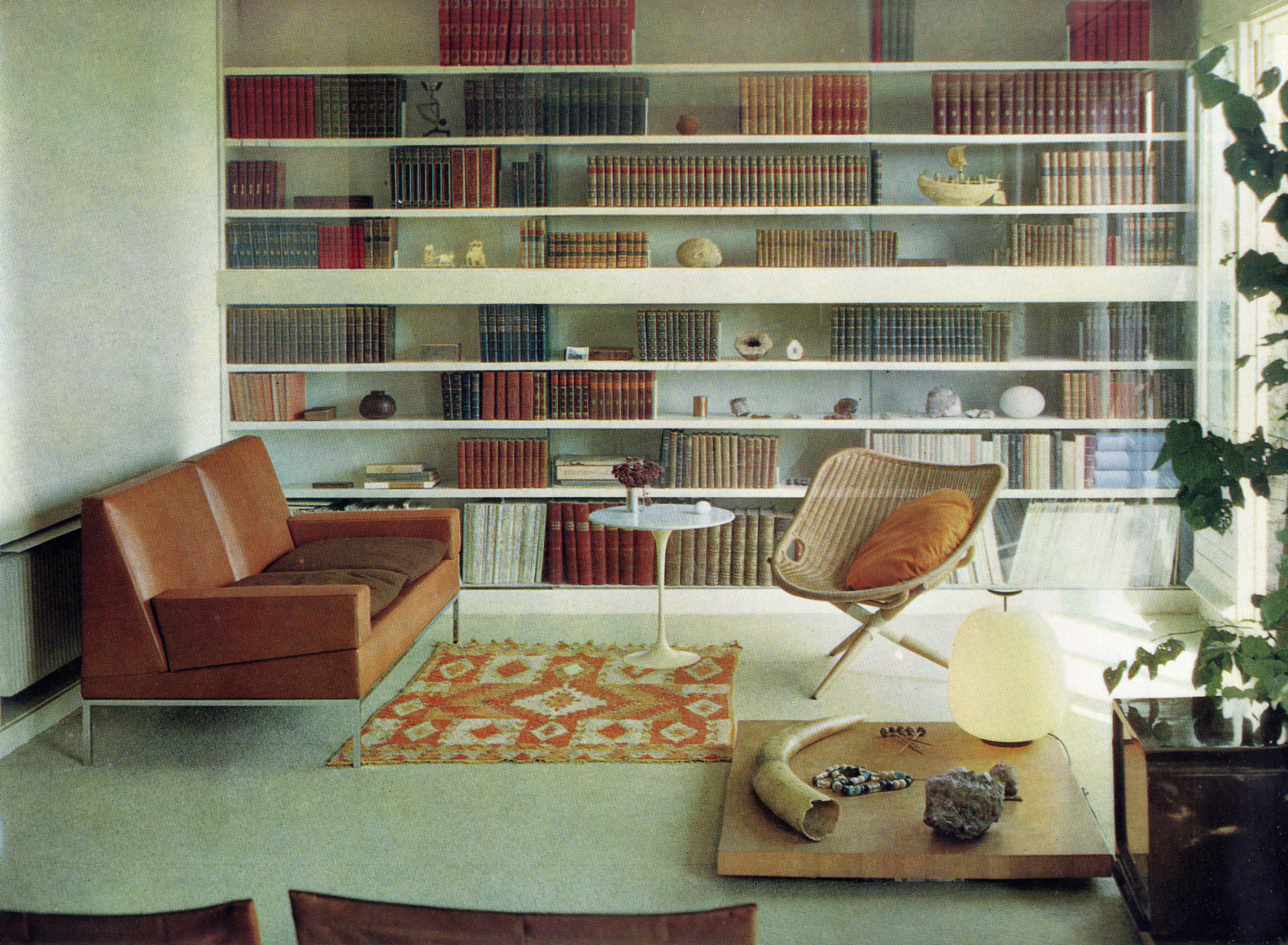 Archival photo of Joseph-Andr&eacute; Motte's apartment with seating area, a low table with various objects, and large bookcase spanning the wall behindbehind