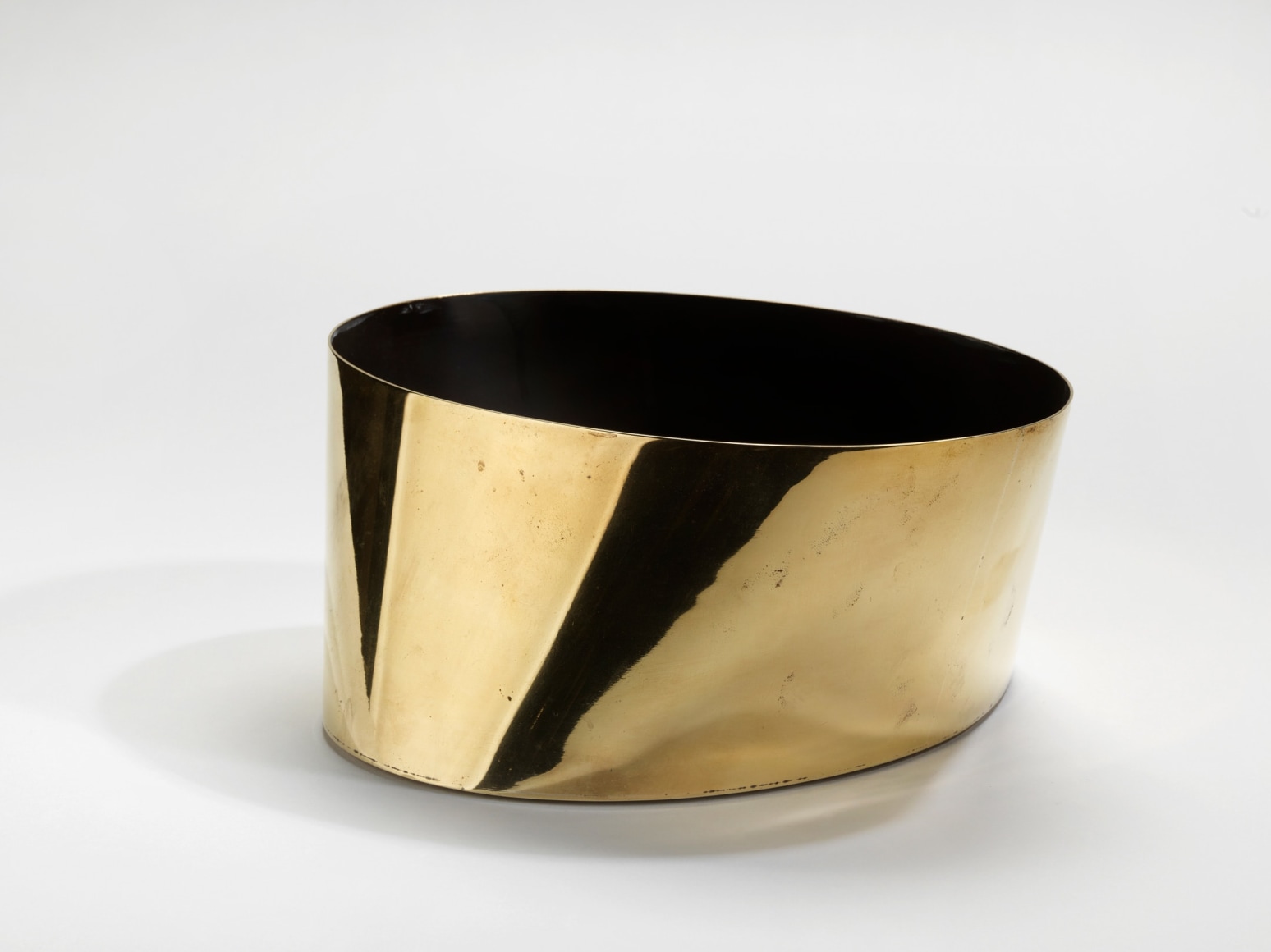 photograph of on circular gold vase with black interiors in a blank room