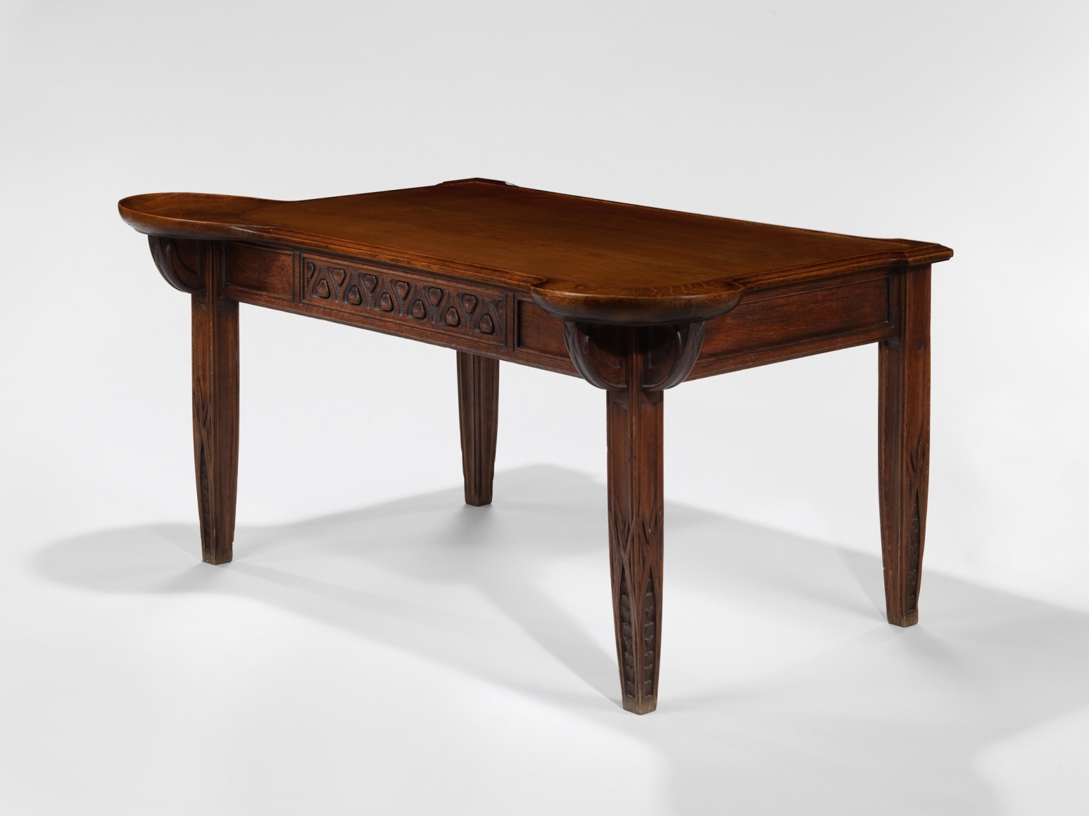 photograph in blank room of desk by Gauthier made in wood with detailing throughout, four legs and drawers.