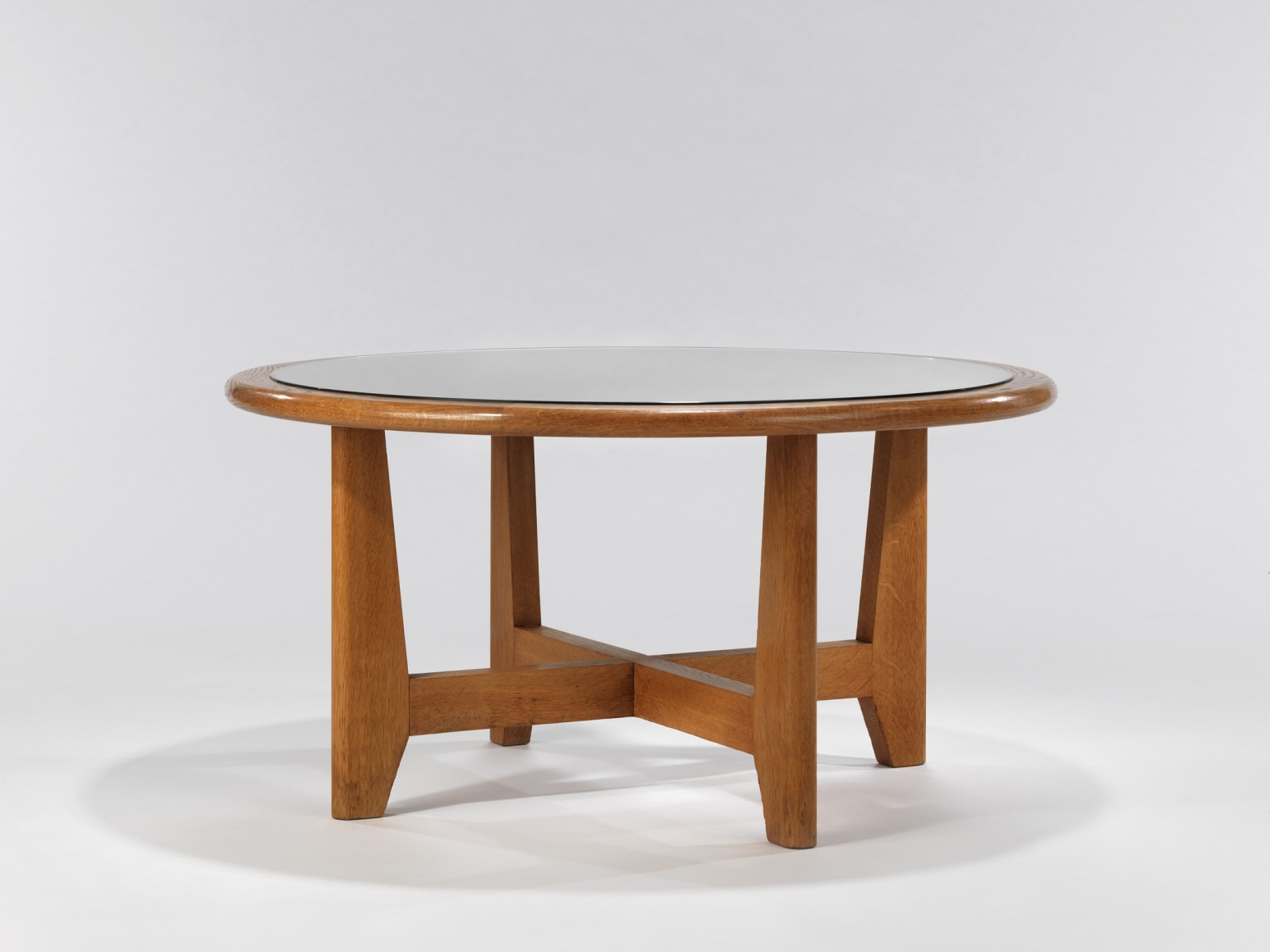 Wooden table with cross base and glass top by Renou and Genniset. View from far away.