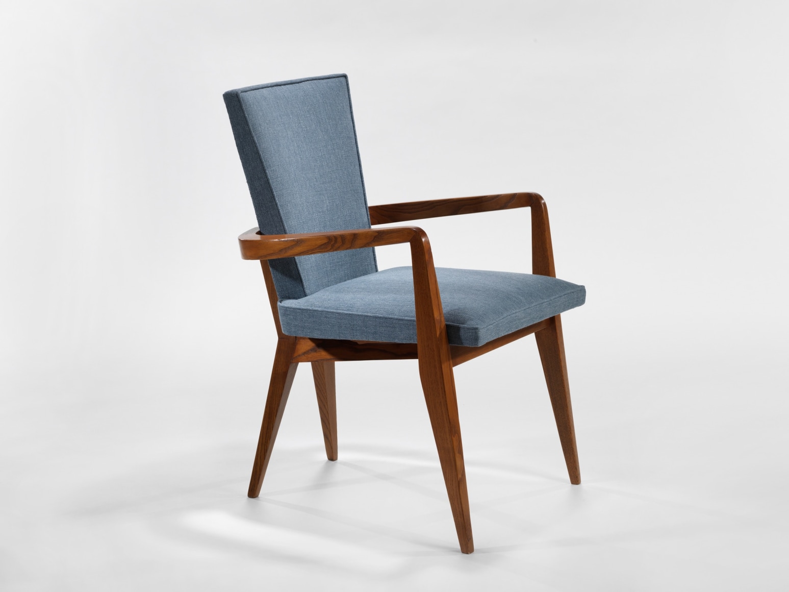 photograph of chair in a blank room with wooden legs and blue upholstery