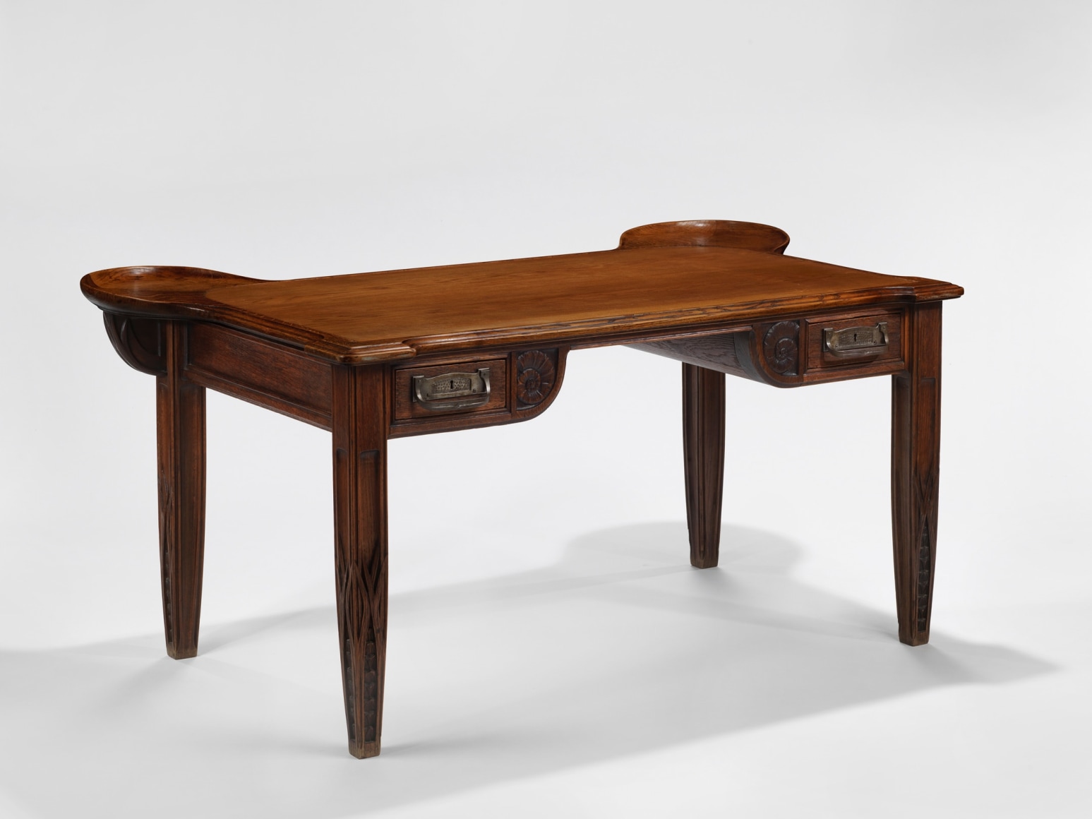 photograph in blank room of desk by Gauthier made in wood with detailing throughout, four legs and drawers.