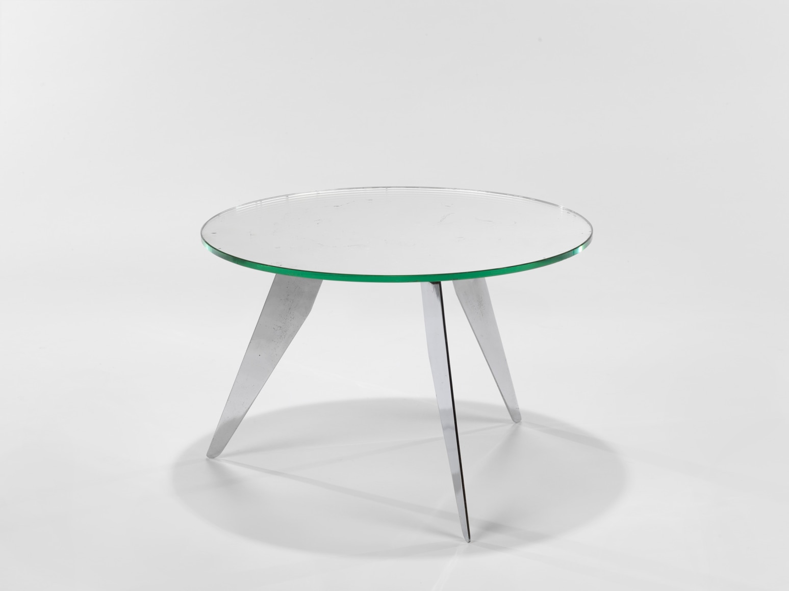 photograph of table in a blank room with metal legs and a glass top