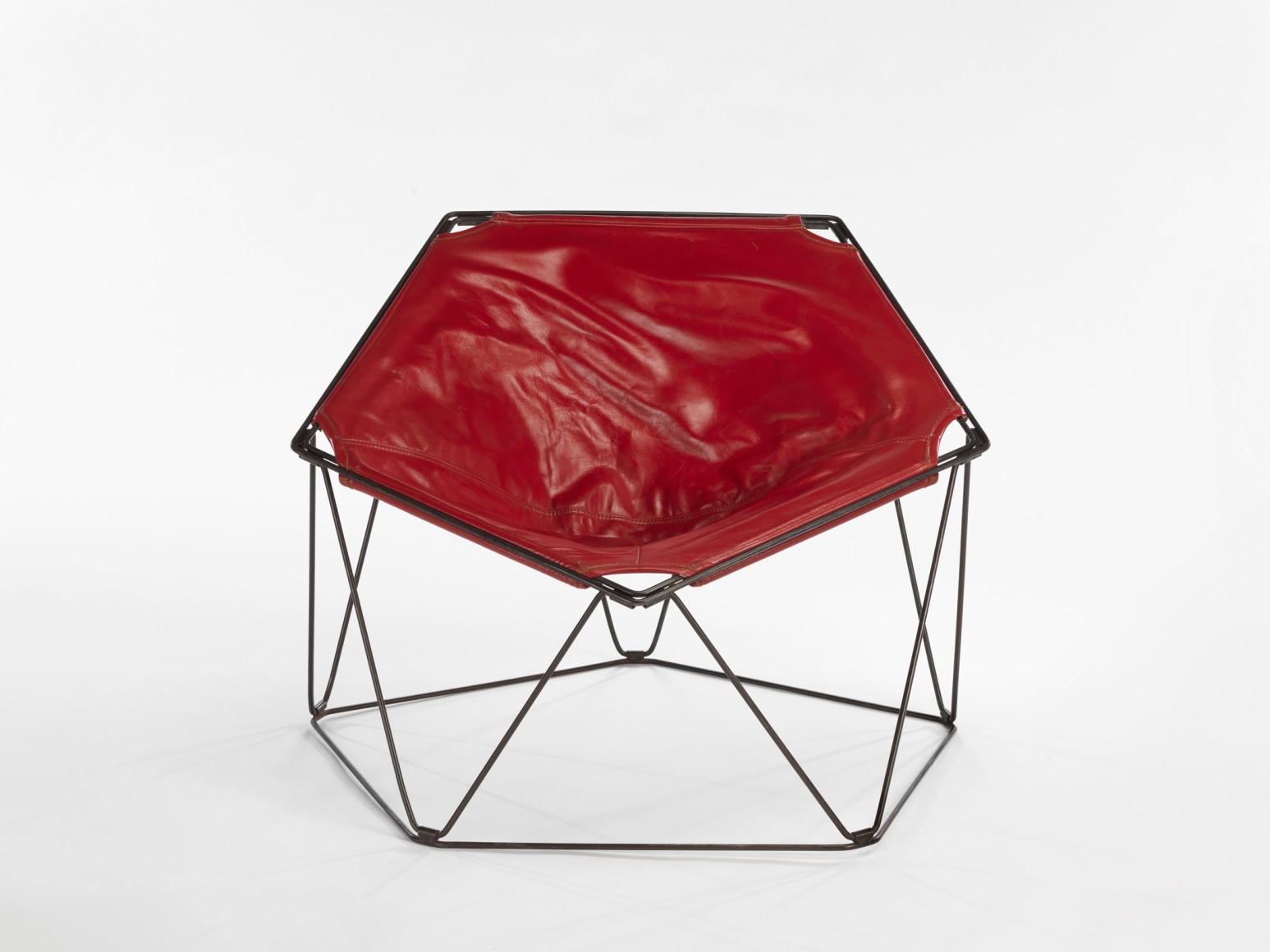 photograph in a blank room of pentagonal shaped chair by Barray with red leather upholstery and black metal wire legs
