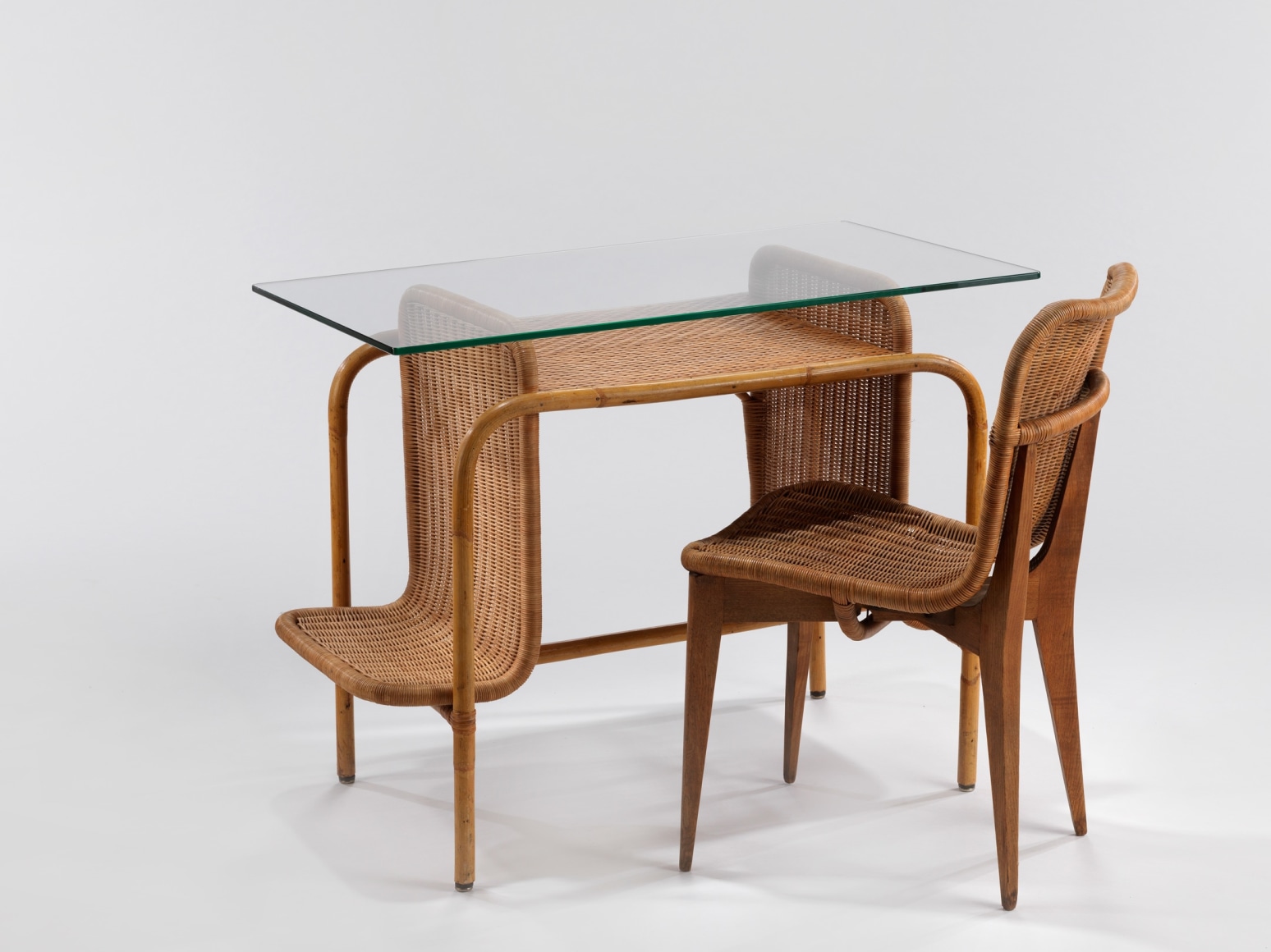 Rattan desk with glass top, pictured with a rattan chair by Louis sognot