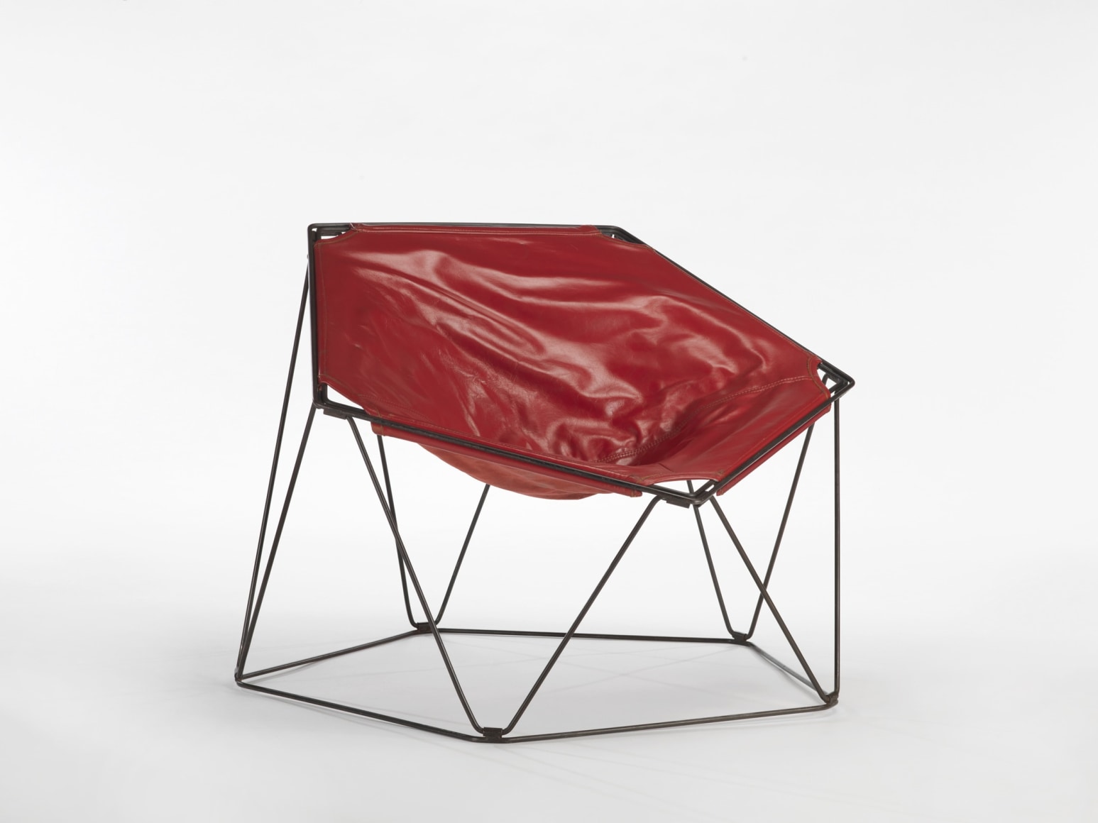 photograph in a blank room of pentagonal shaped chair by Barray with red leather upholstery and black metal wire legs